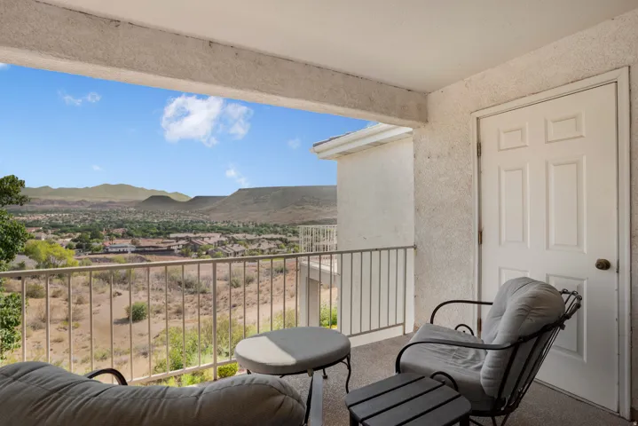 Spacious balcony featuring a metal railing, stucco exterior, and painted panel door, all overlooking a distant mountainous landscape and expansive natural terrain