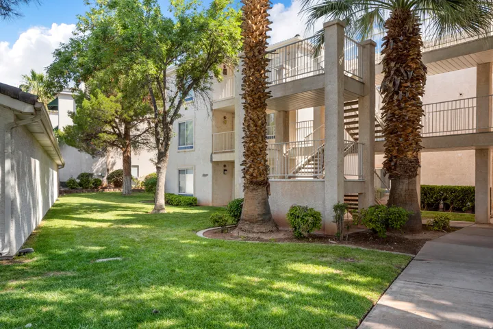 Mature landscaping with established trees and palm trees, a manicured lawn, and multi-story buildings featuring balconies with railings