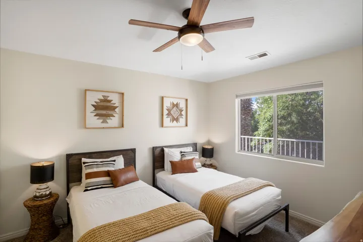 Spacious room featuring a ceiling fan with integrated lighting, wood-finish headboards, and ample natural light from a large window