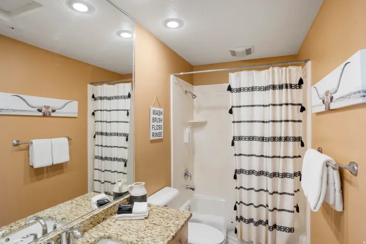 Bathroom featuring a bathtub with shower, recessed lighting, a stone-finish countertop, and a vanity mirror