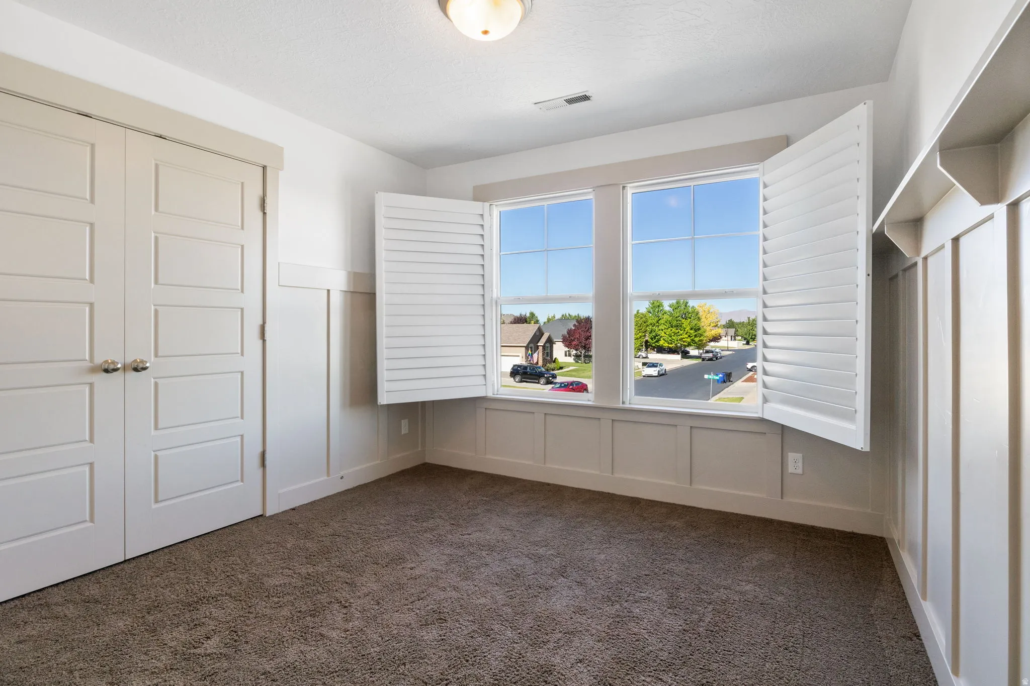 Bright room featuring twin windows with white plantation shutters, board and batten wall detailing, and soft brown carpeting