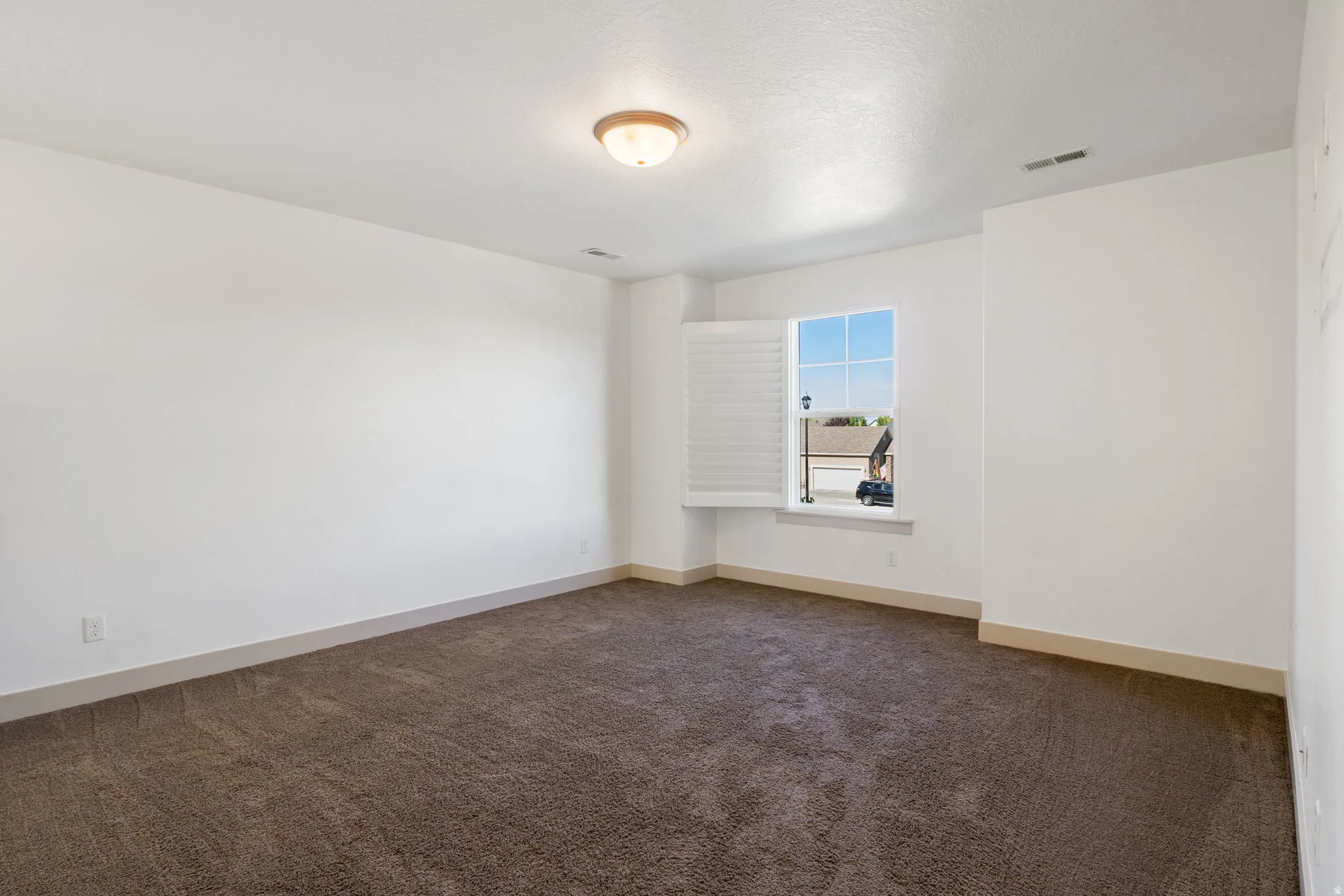 Spacious room featuring neutral paint, brown carpeting, a ceiling-mounted light fixture, and a window with white blinds