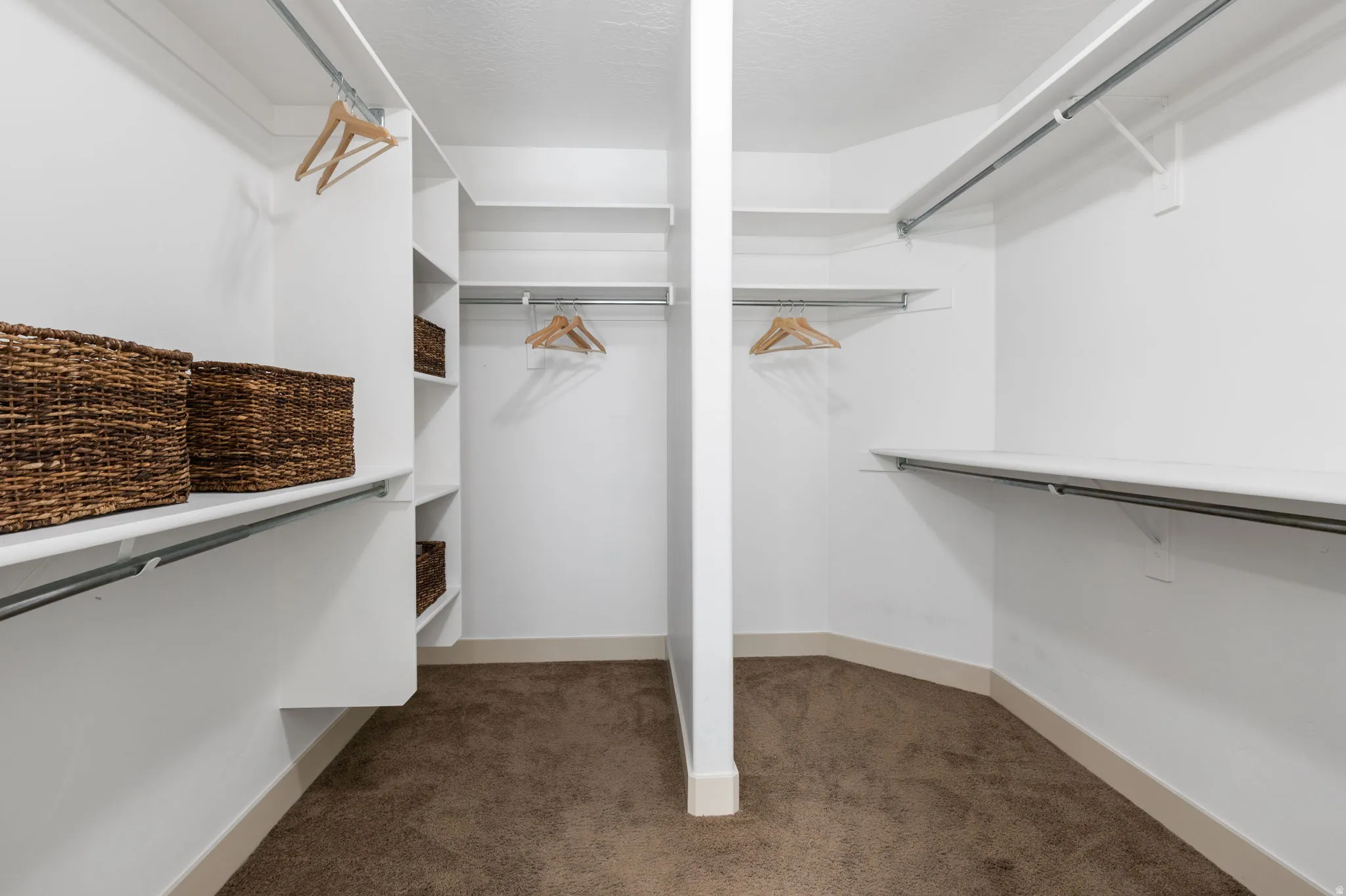 Spacious walk-in closet featuring white built-in shelving, chrome hanging rods, and a neutral-toned carpet