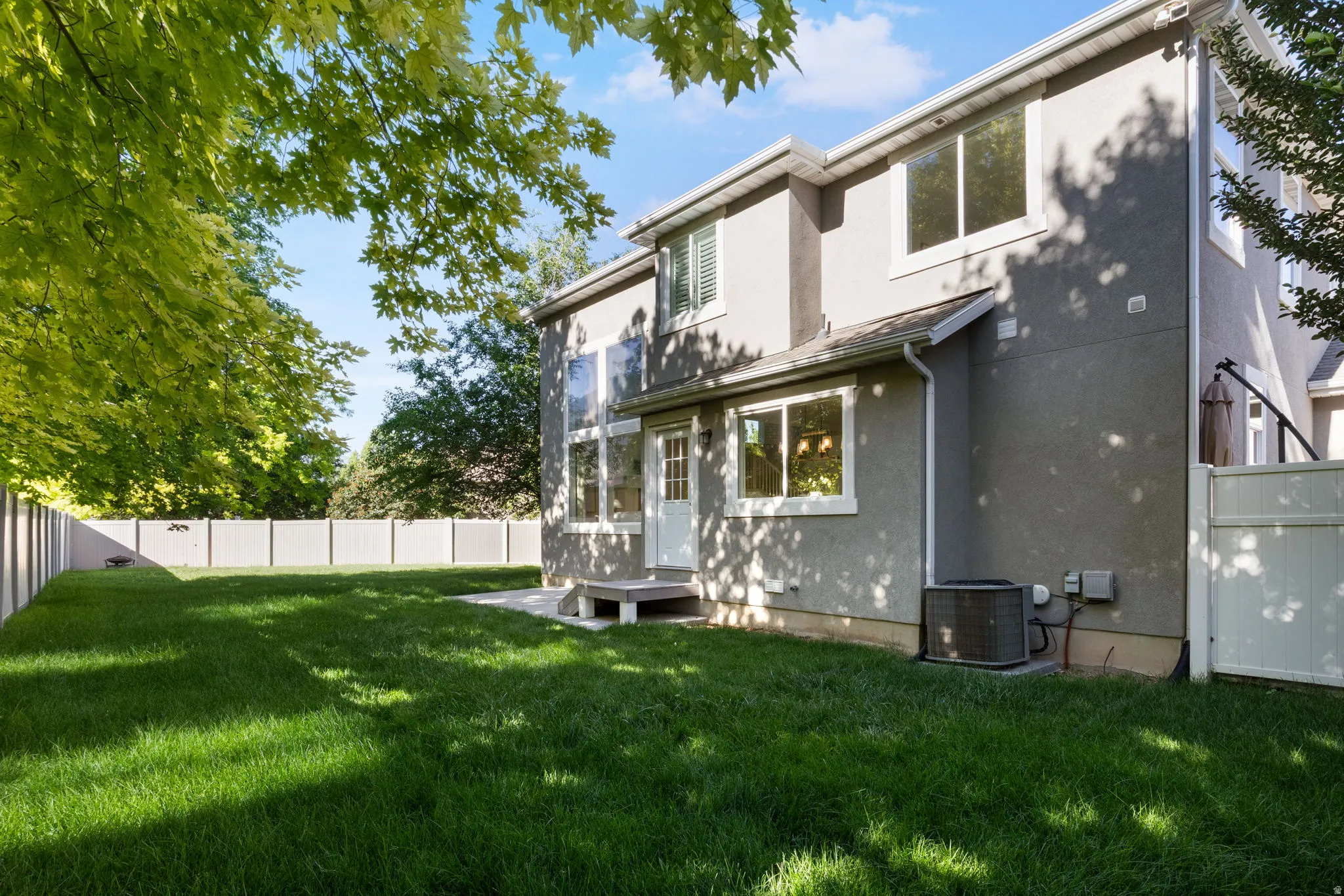 Expansive backyard featuring a manicured lawn, concrete patio, and mature trees