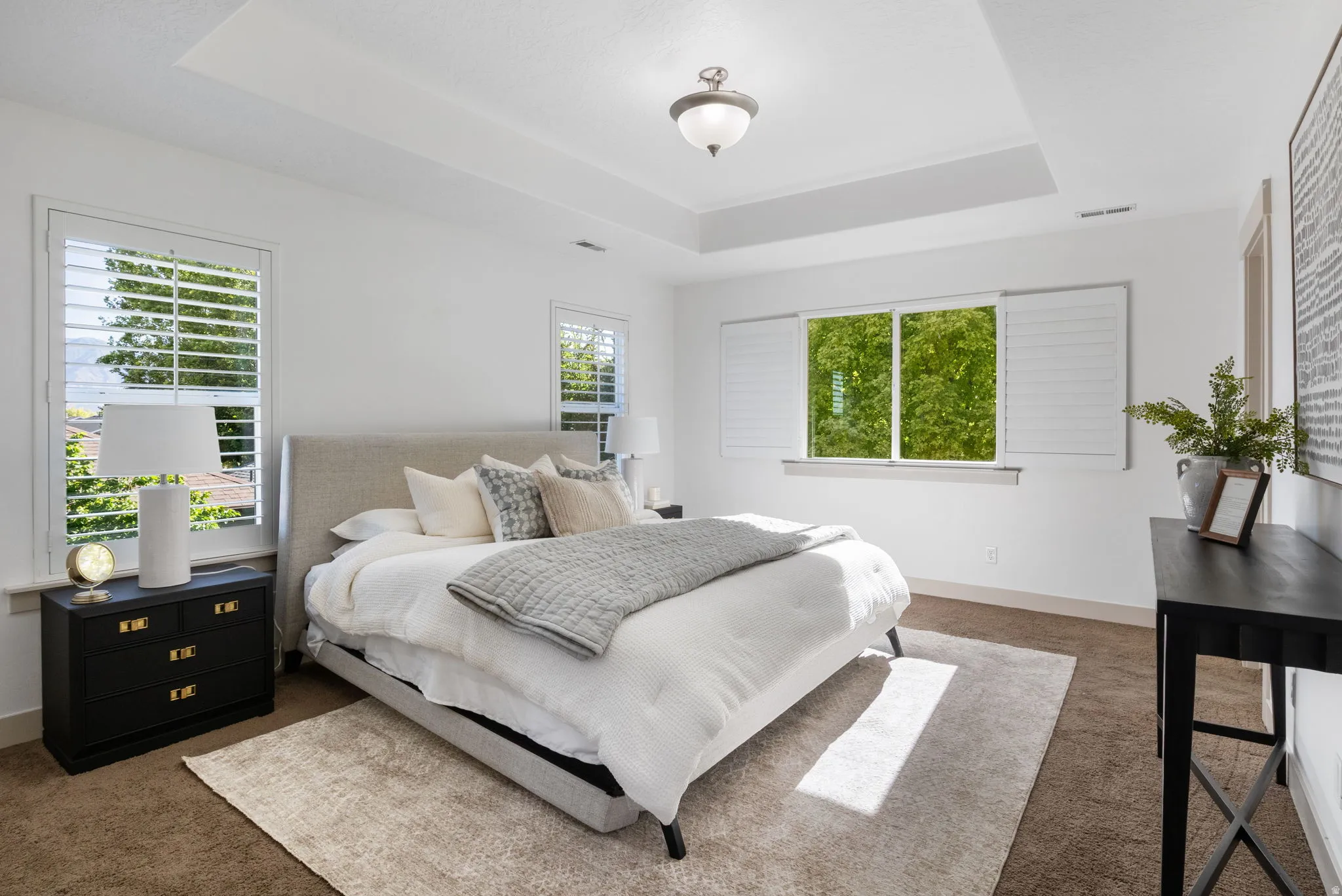 Spacious room featuring a tray ceiling, recessed lighting, and multiple windows with plantation shutters