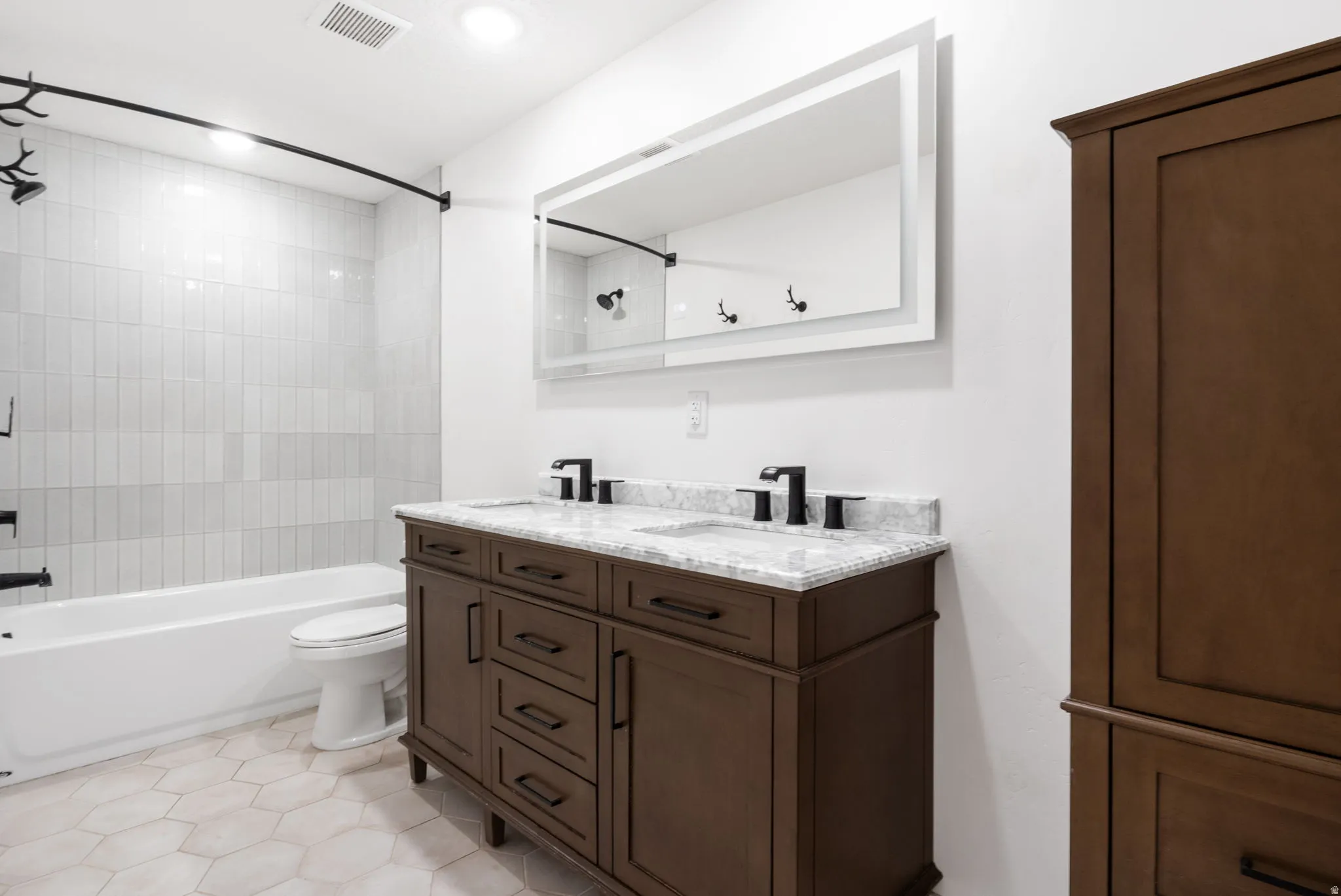 Bathroom featuring a dual-sink vanity with a light-toned countertop, black fixtures, and framed mirror