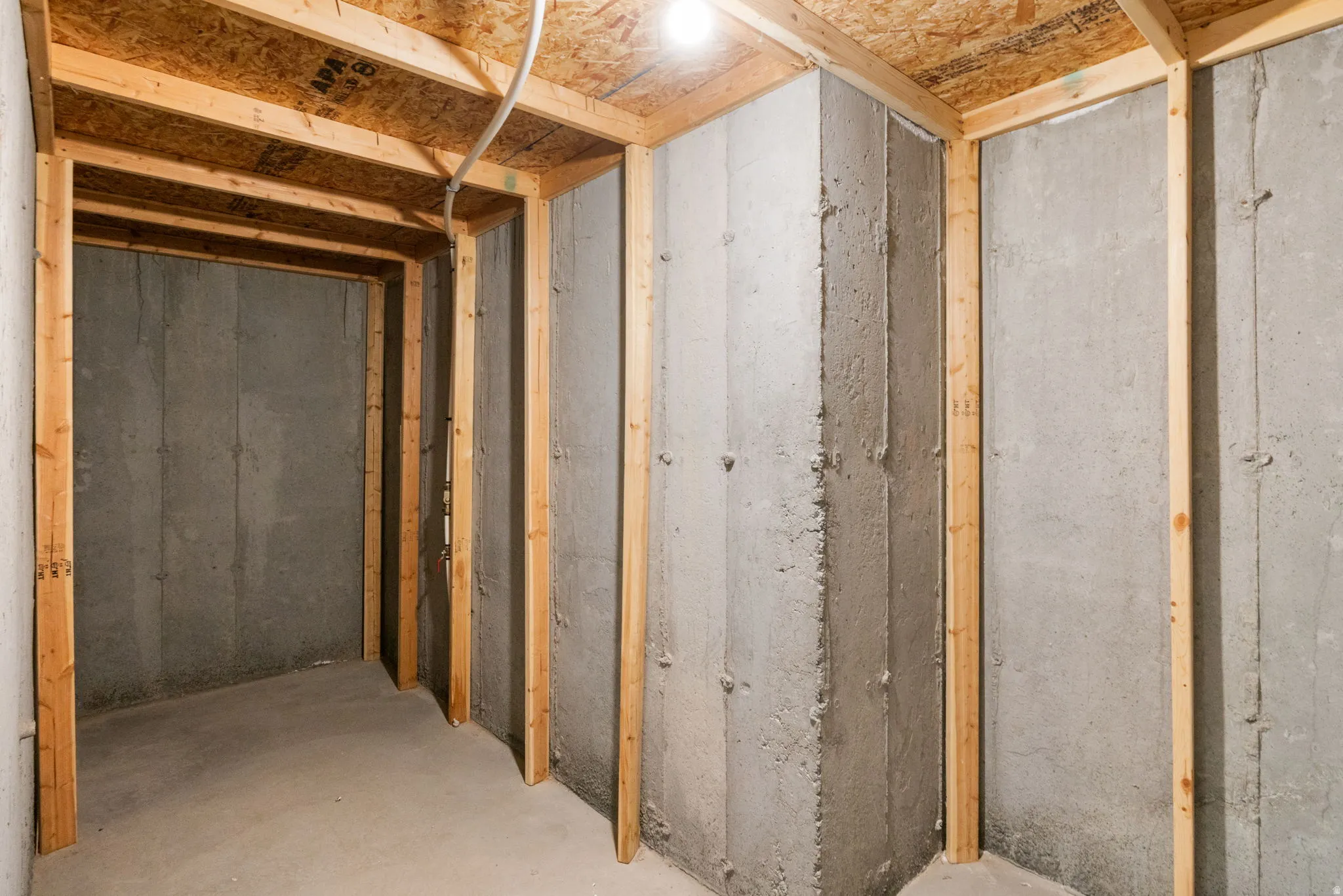 Unfinished basement space featuring concrete walls, wood framing, and exposed OSB subfloor