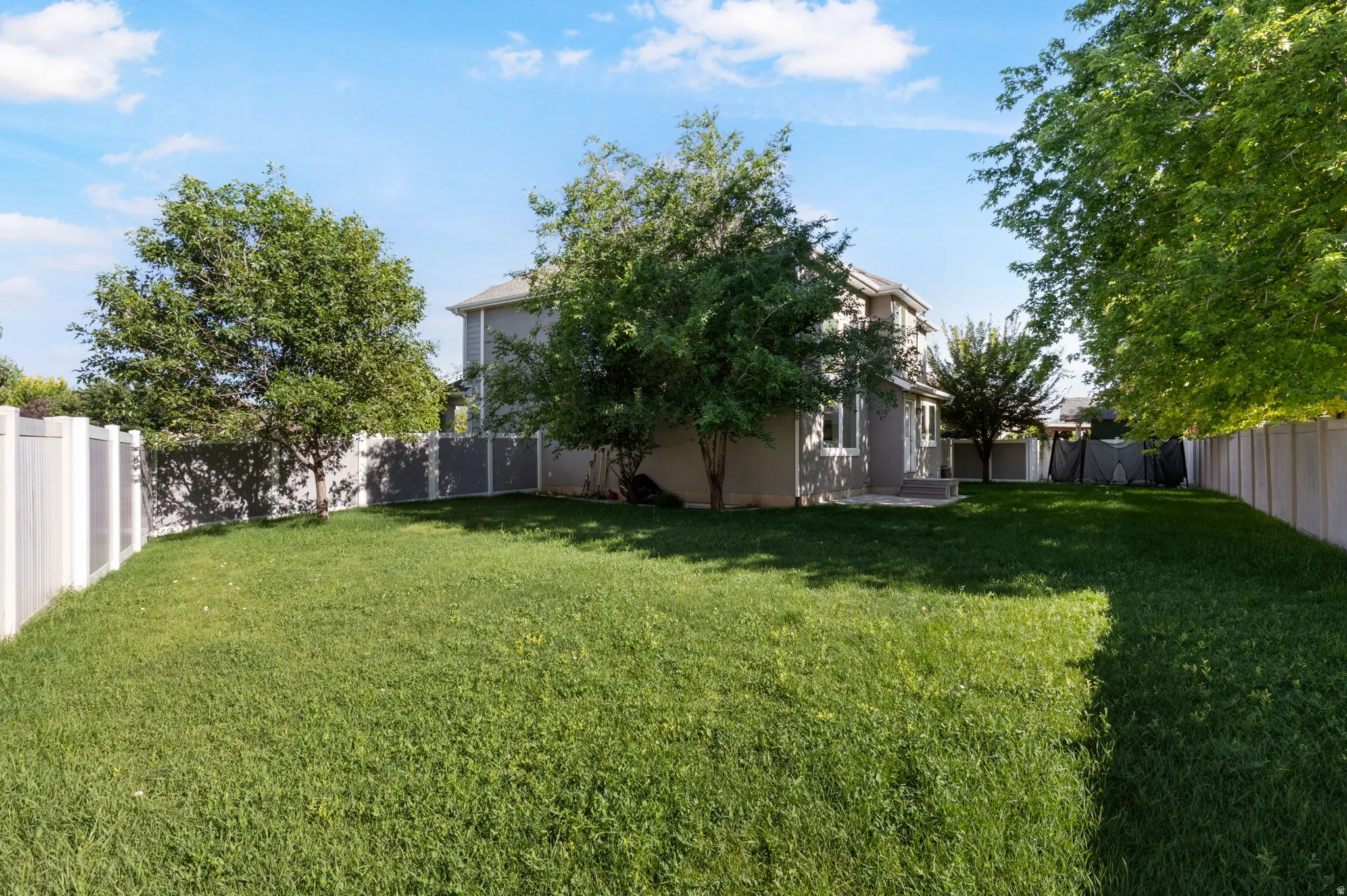 Expansive green lawn with mature trees and a two-story gray stucco exterior