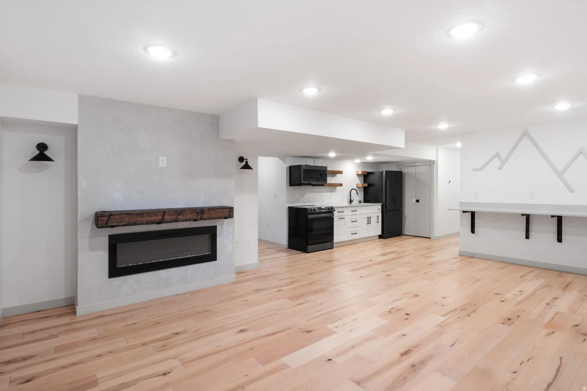 Open-concept living area featuring light wood-finish flooring, recessed lighting, and a modern linear fireplace with a substantial wood mantel