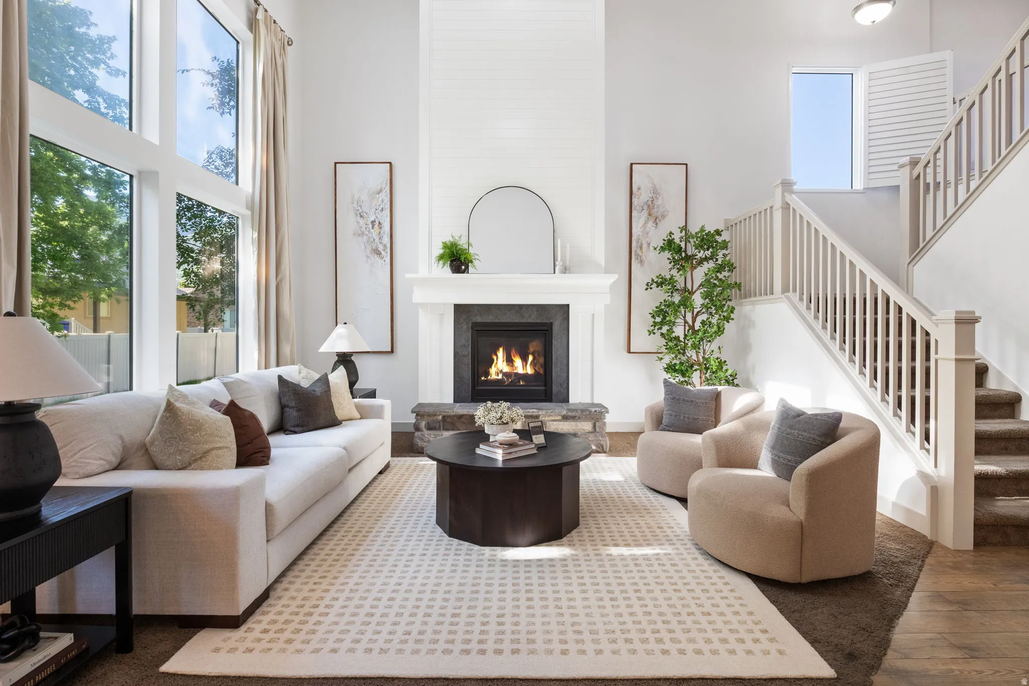 Two-story living area featuring tall windows, a shiplap fireplace with stone hearth, a staircase with white balusters, and a light-colored area rug over carpeting