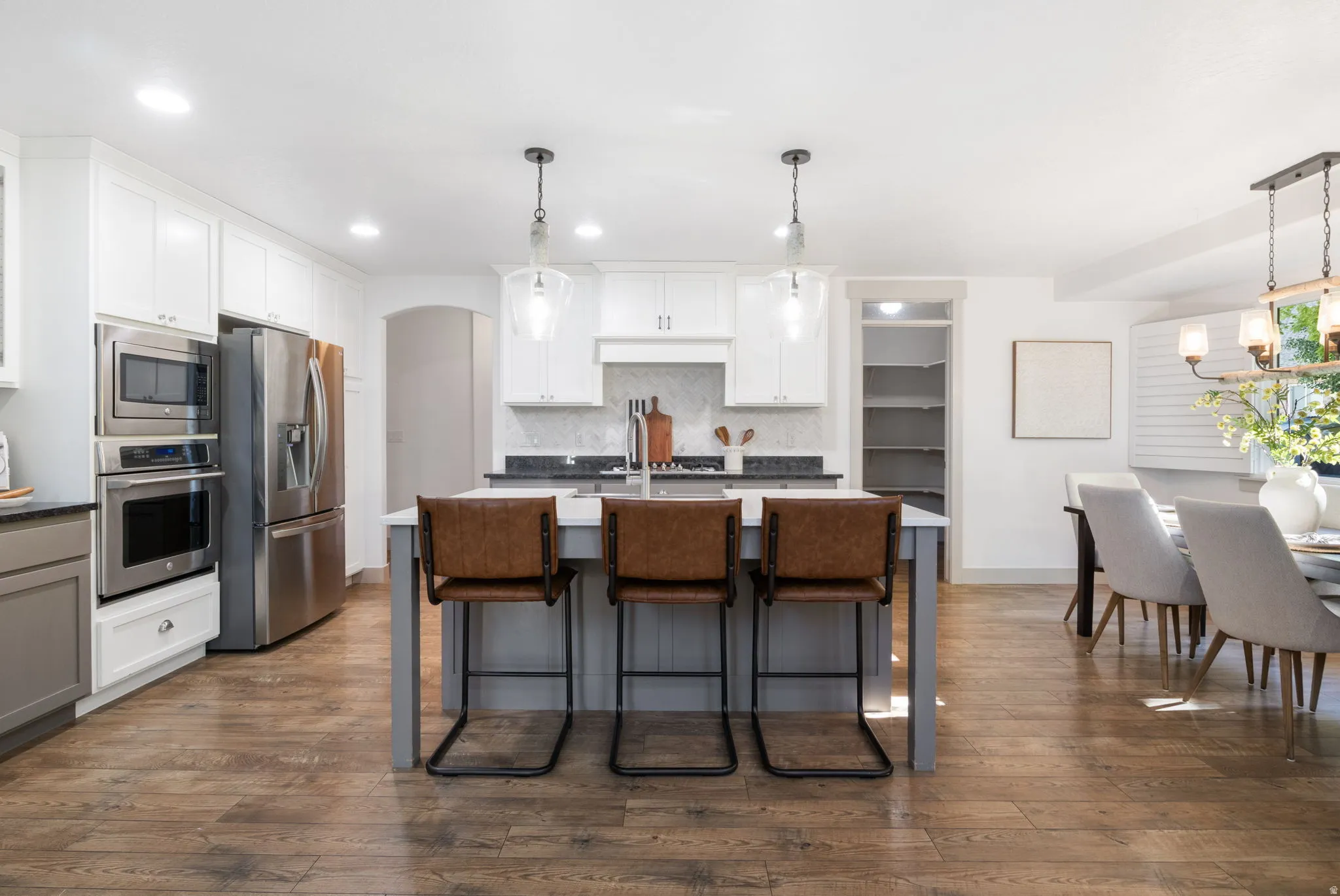 Gourmet kitchen featuring a central island with seating, stainless steel appliances, white upper cabinetry, a patterned tile backsplash, and wood-finish flooring