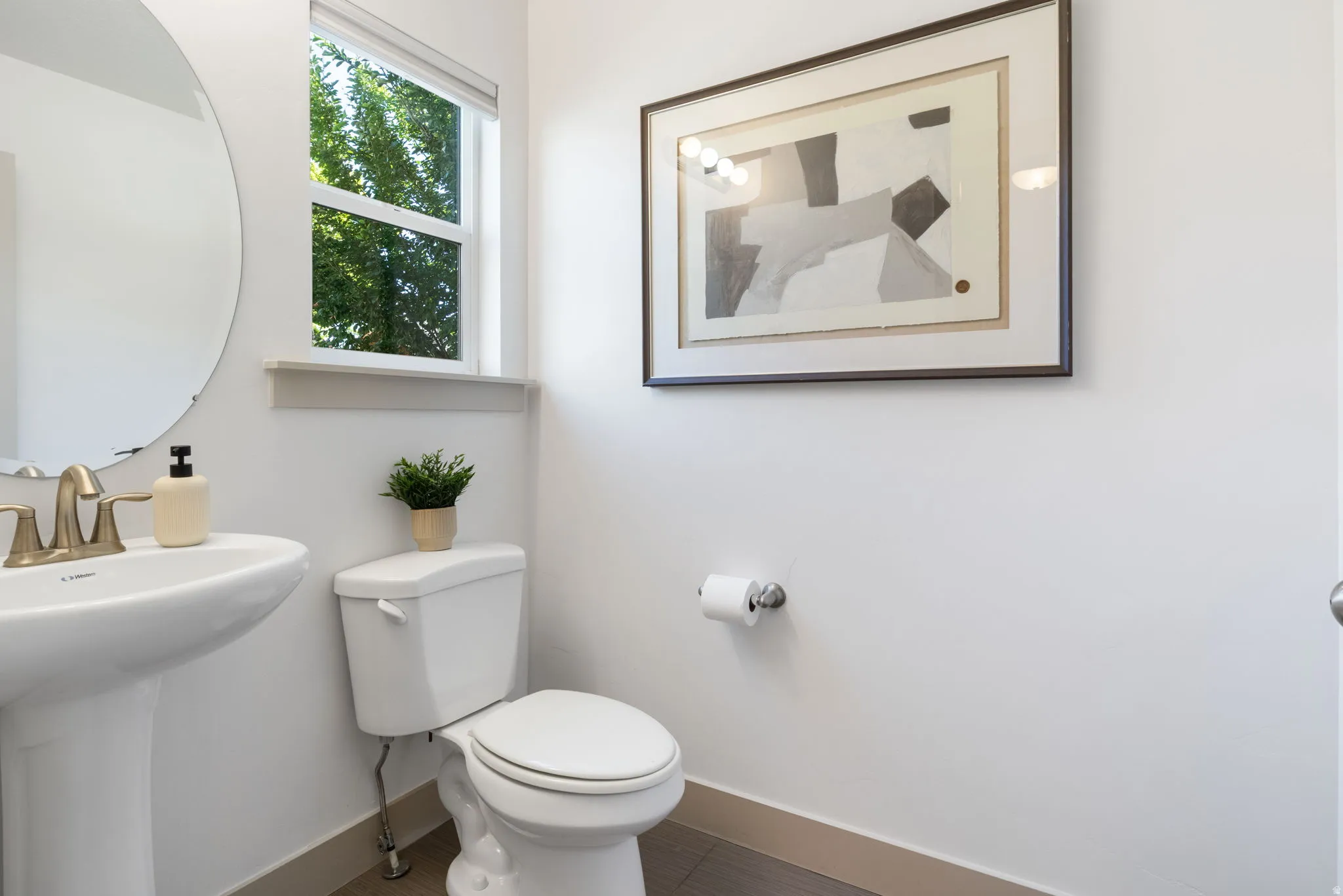 Pedestal sink with brass-finish faucet, oval mirror, and window