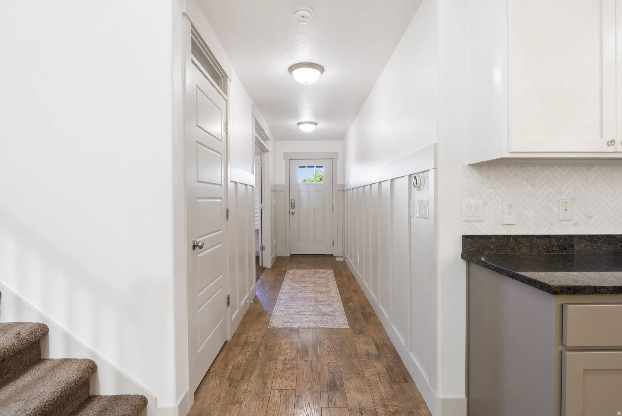 Entryway hall featuring wood-finish flooring, white board and batten wall detailing, and a paneled entry door with frosted glass