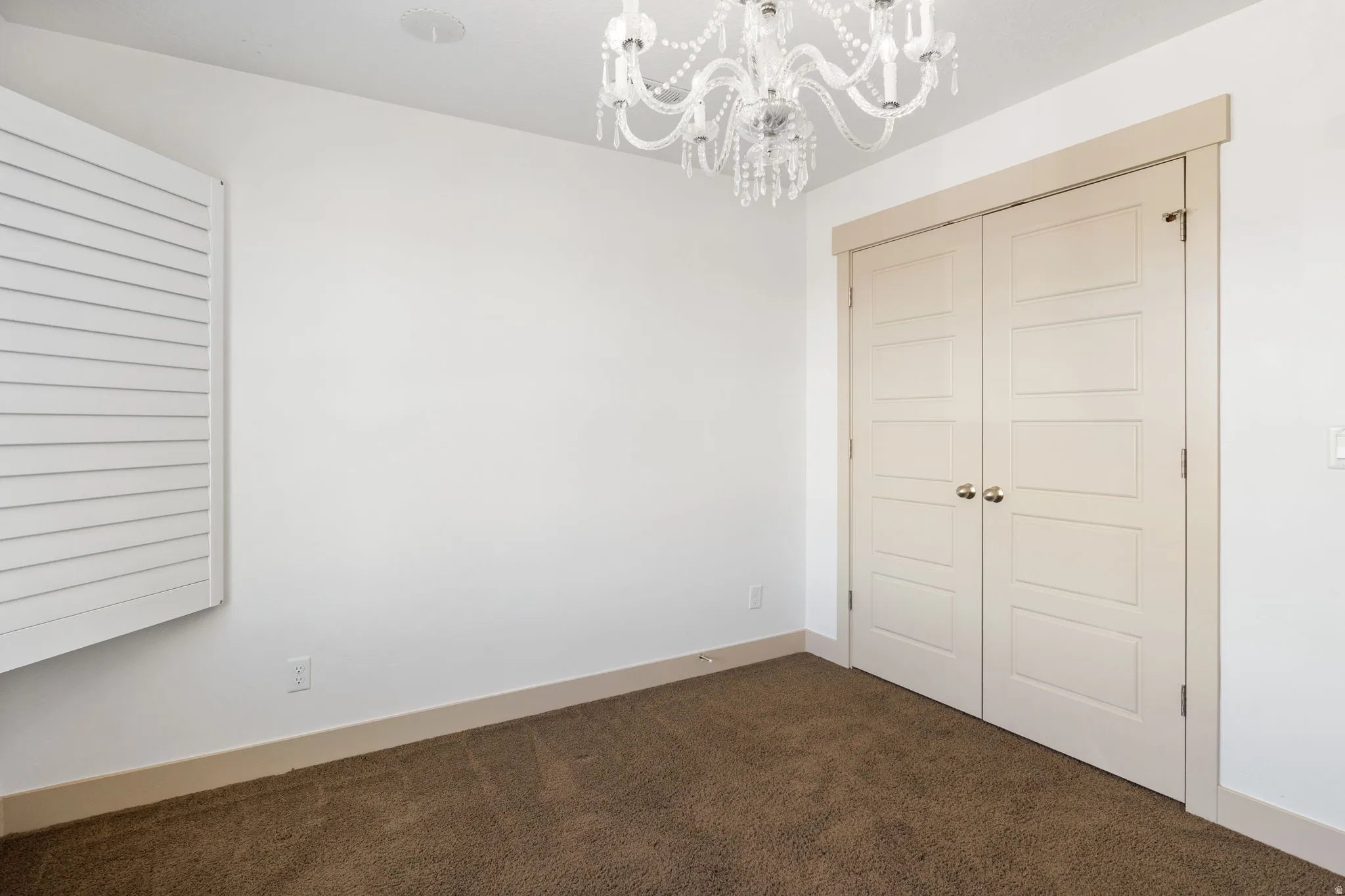 Bright room featuring white walls, brown carpet, and a decorative chandelier