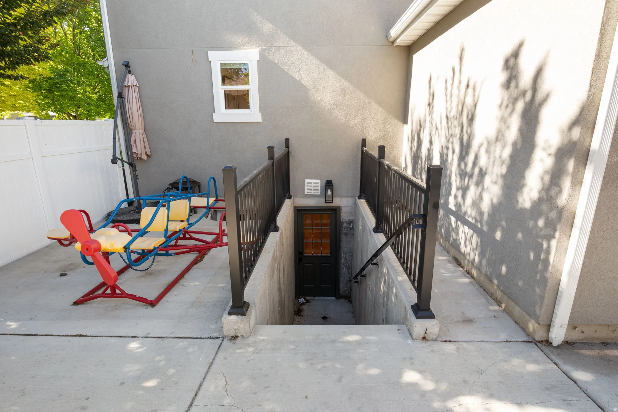 Exterior entrance with a basement door, featuring black metal railings and concrete steps