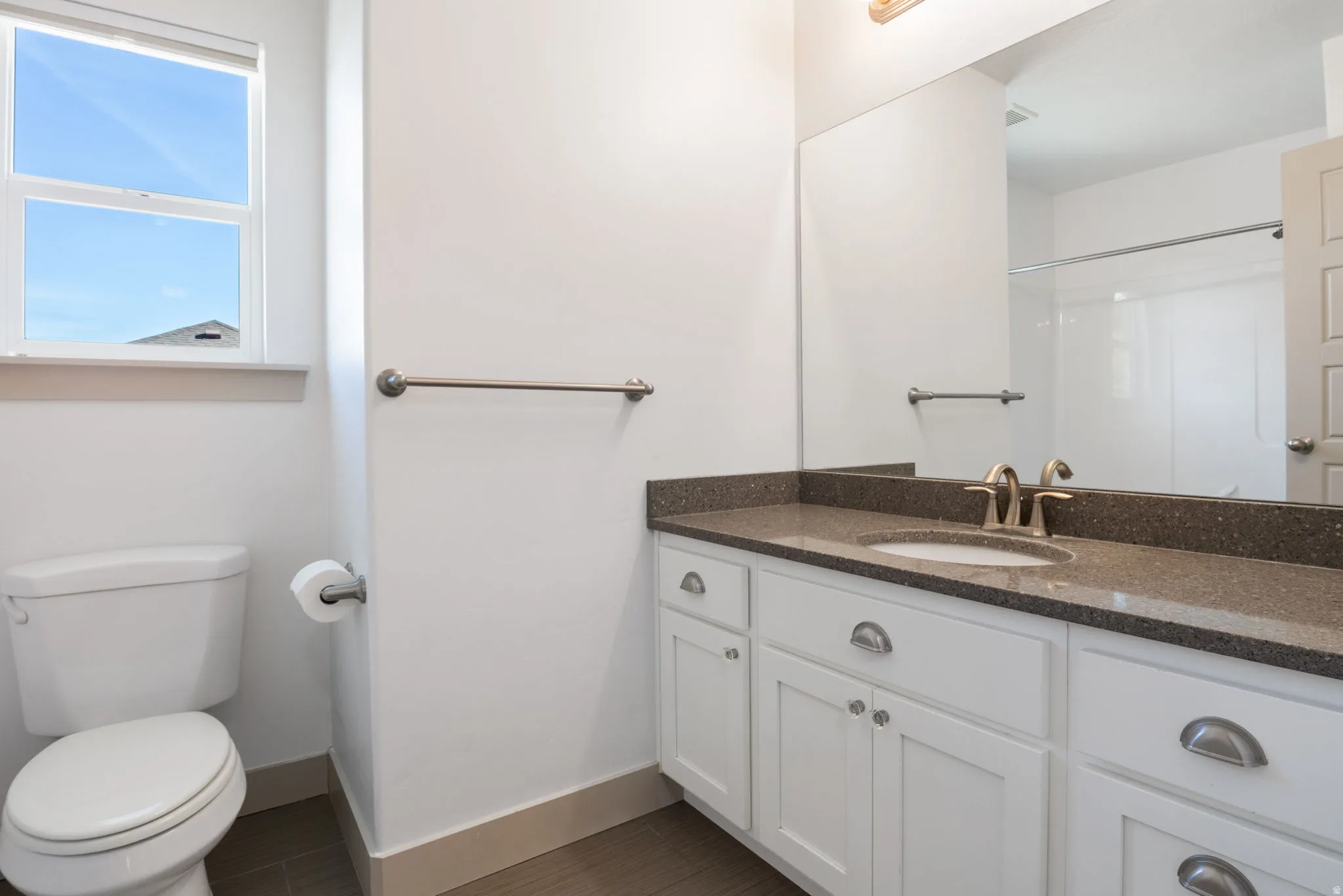 Bathroom featuring a single vanity with white cabinetry, a dark speckled countertop, and brushed nickel hardware