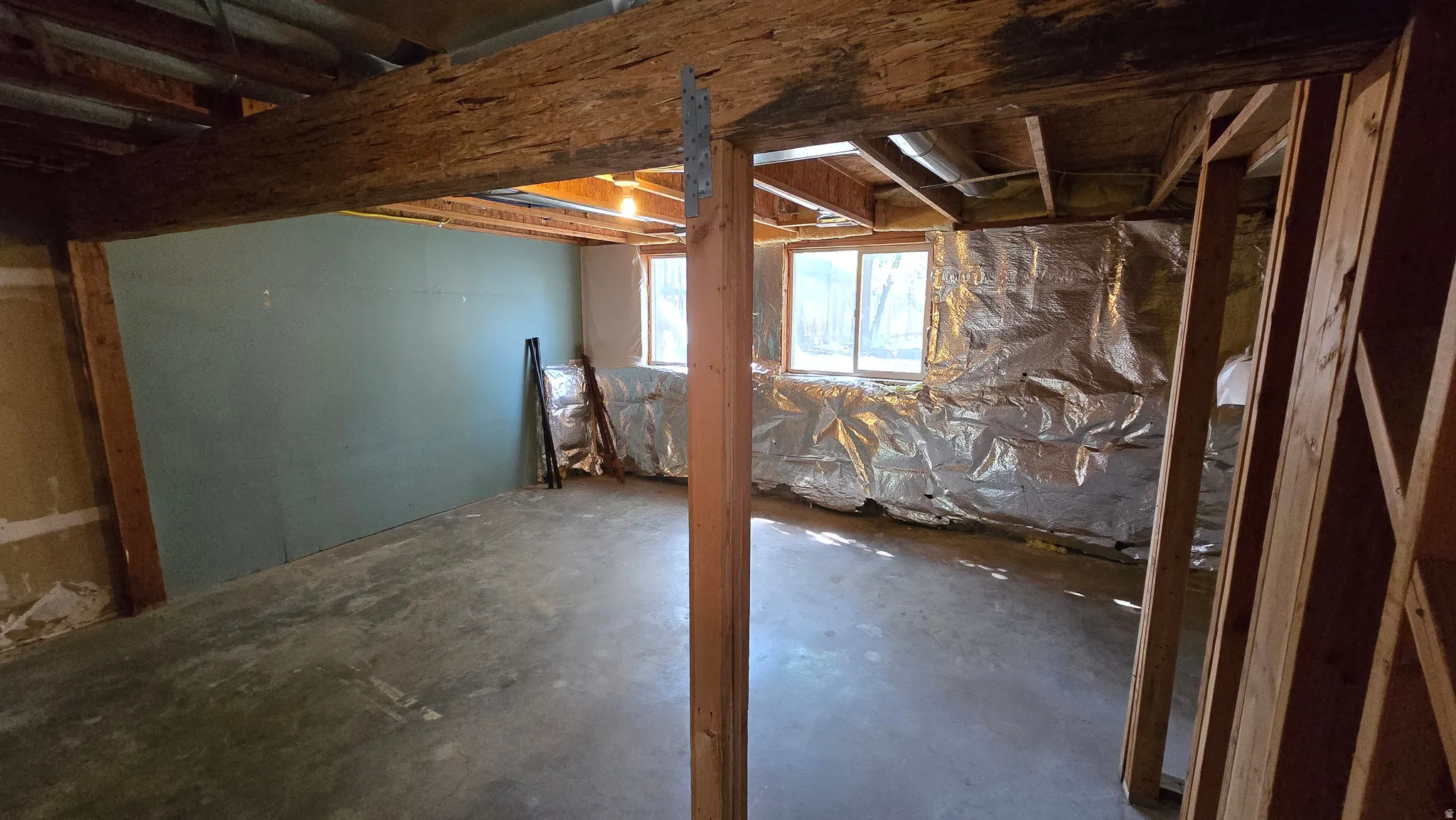 Unfinished basement with concrete flooring, exposed wood framing, and multiple windows