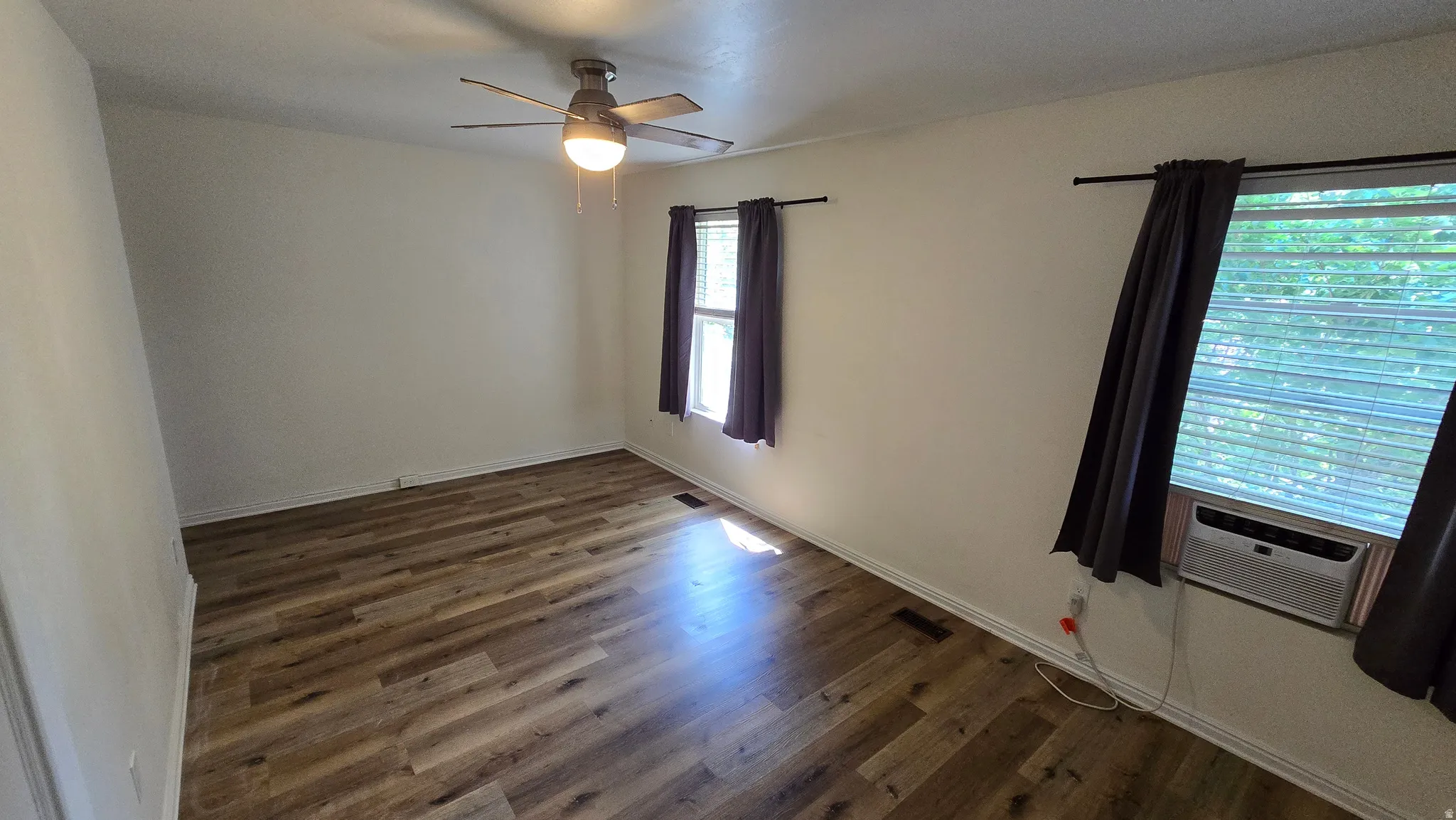 Wood-finish flooring, ceiling fan with integrated lighting, window-mounted air conditioning unit, and multiple windows