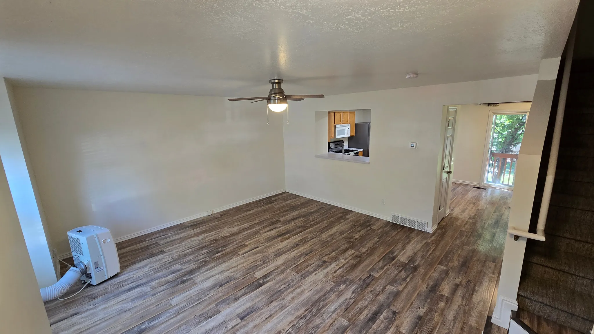 Wood-finish flooring throughout, ceiling fan with integrated lighting, pass-through window, and a door leading to an exterior balcony