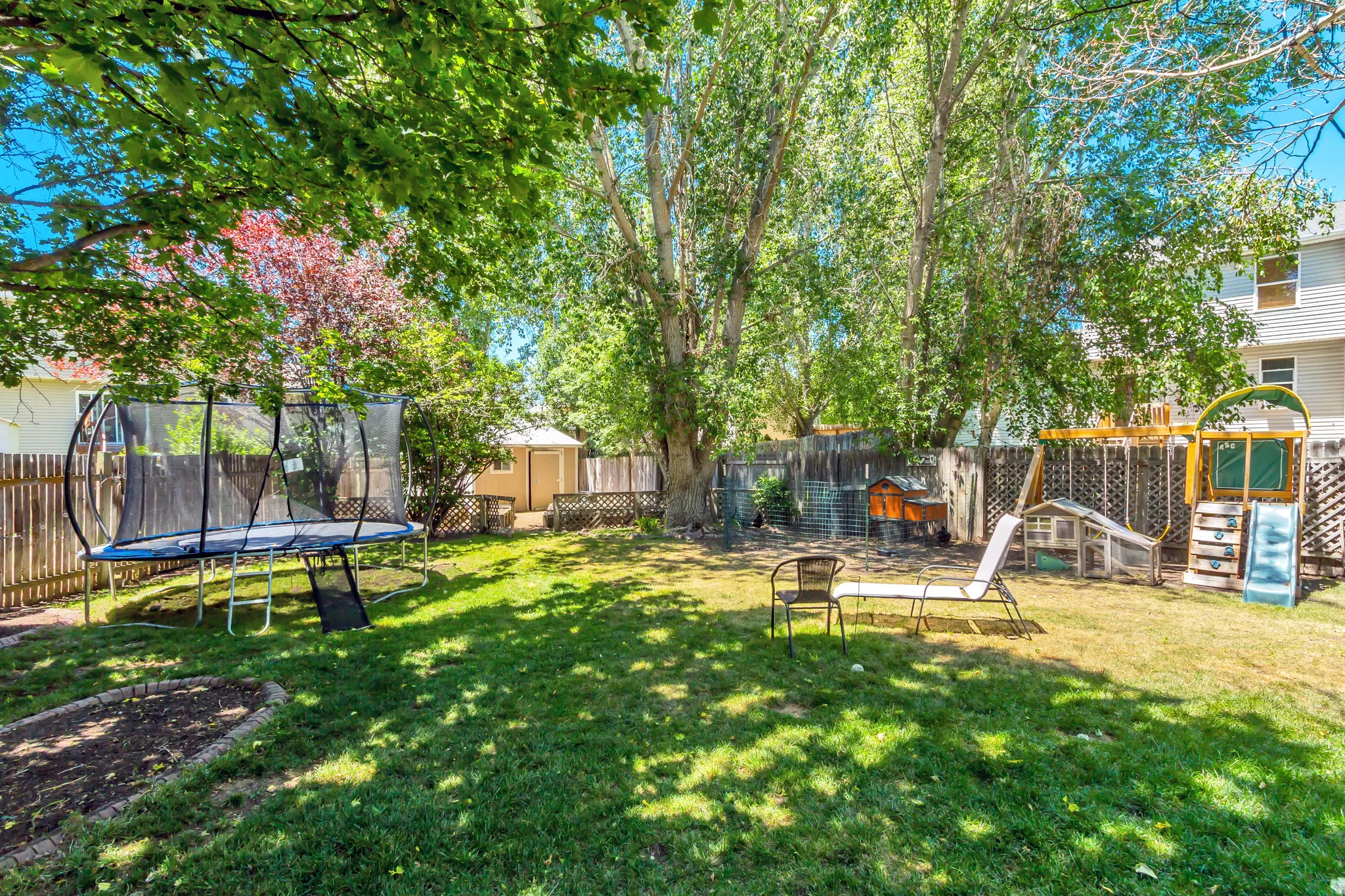 Expansive grassy backyard featuring a perimeter fence, mature trees, and a ground-level planting bed
