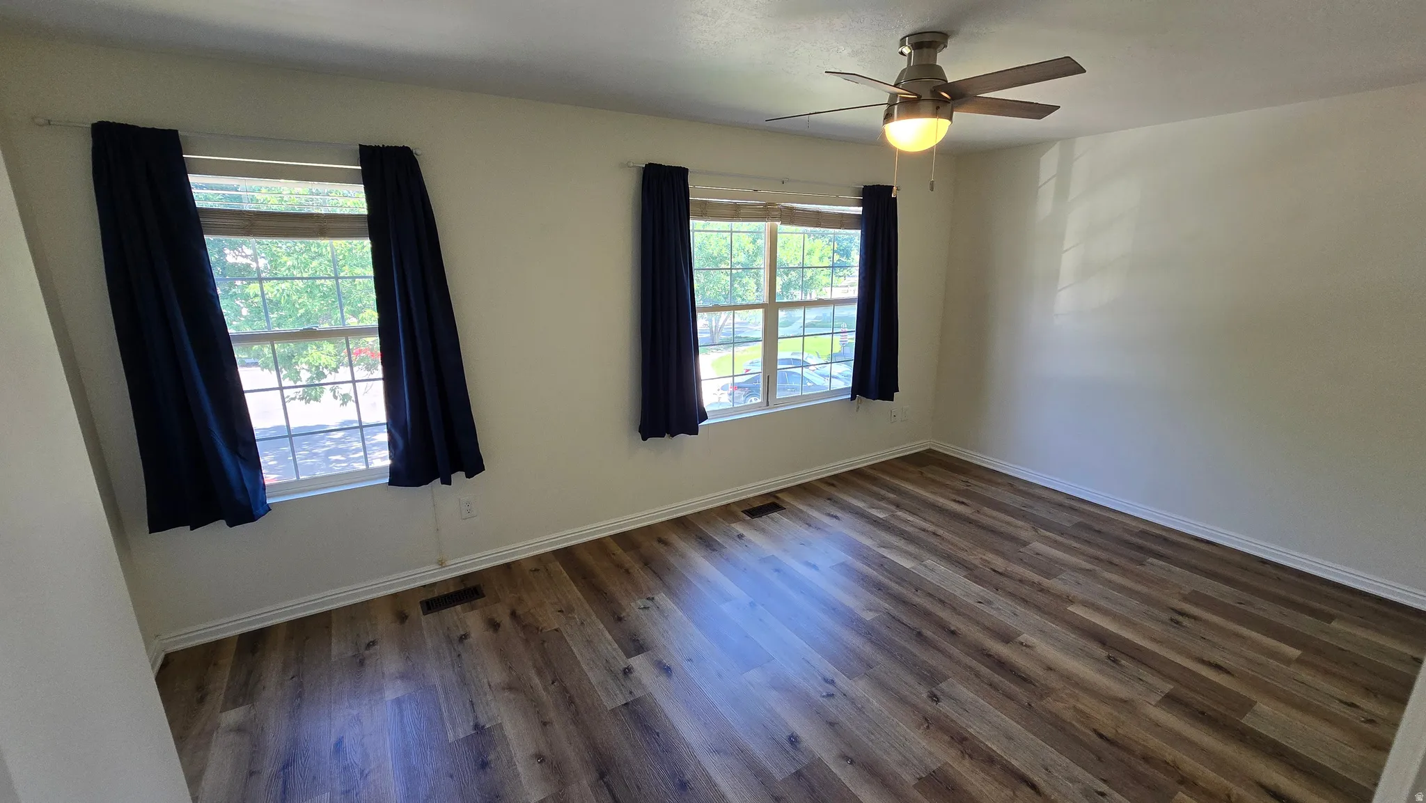 Spacious room with wood-finish flooring, multiple windows, and a ceiling fan with integrated lighting