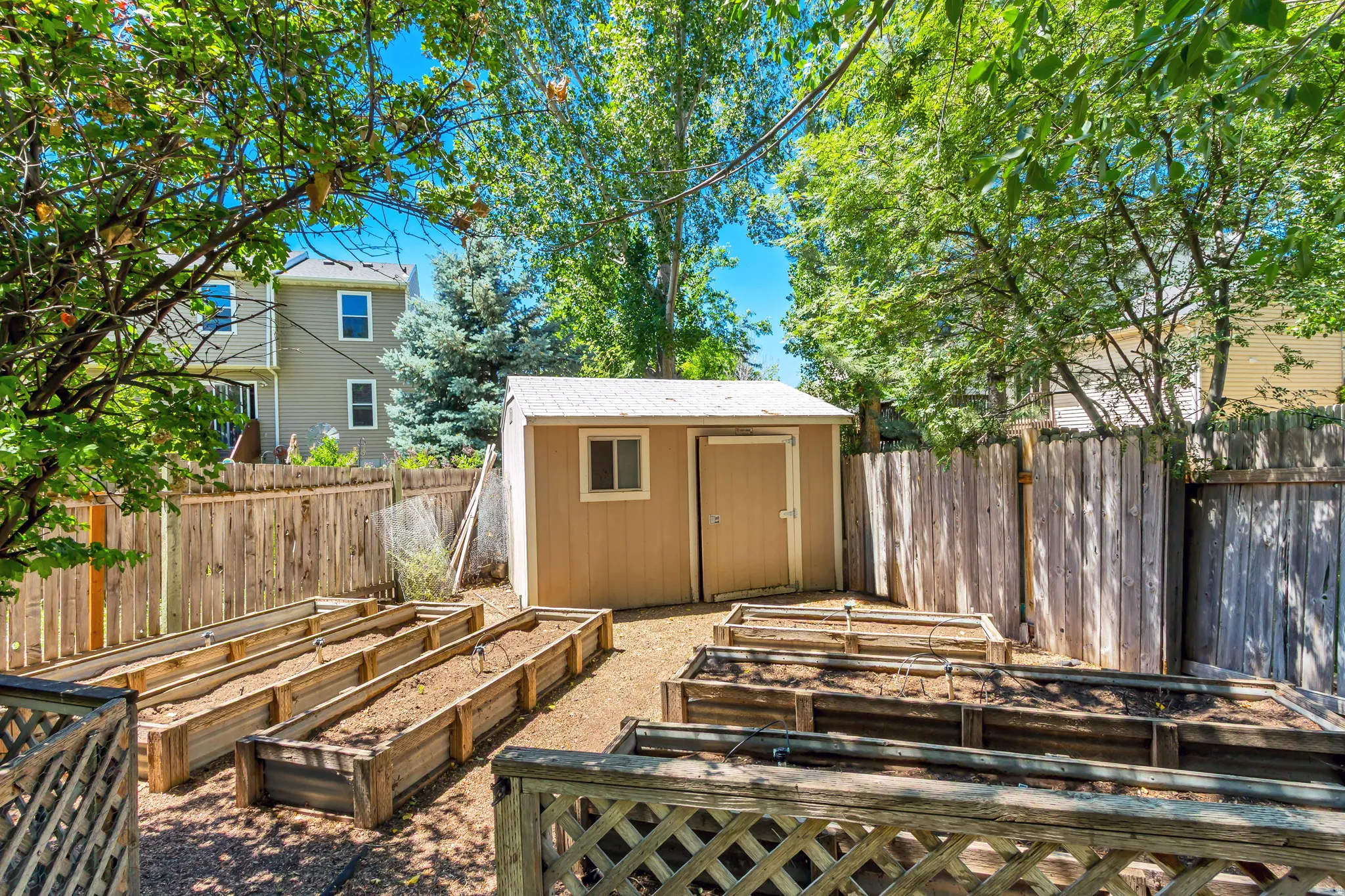 Backyard featuring multiple raised garden beds, a storage shed with a window, and wood fencing