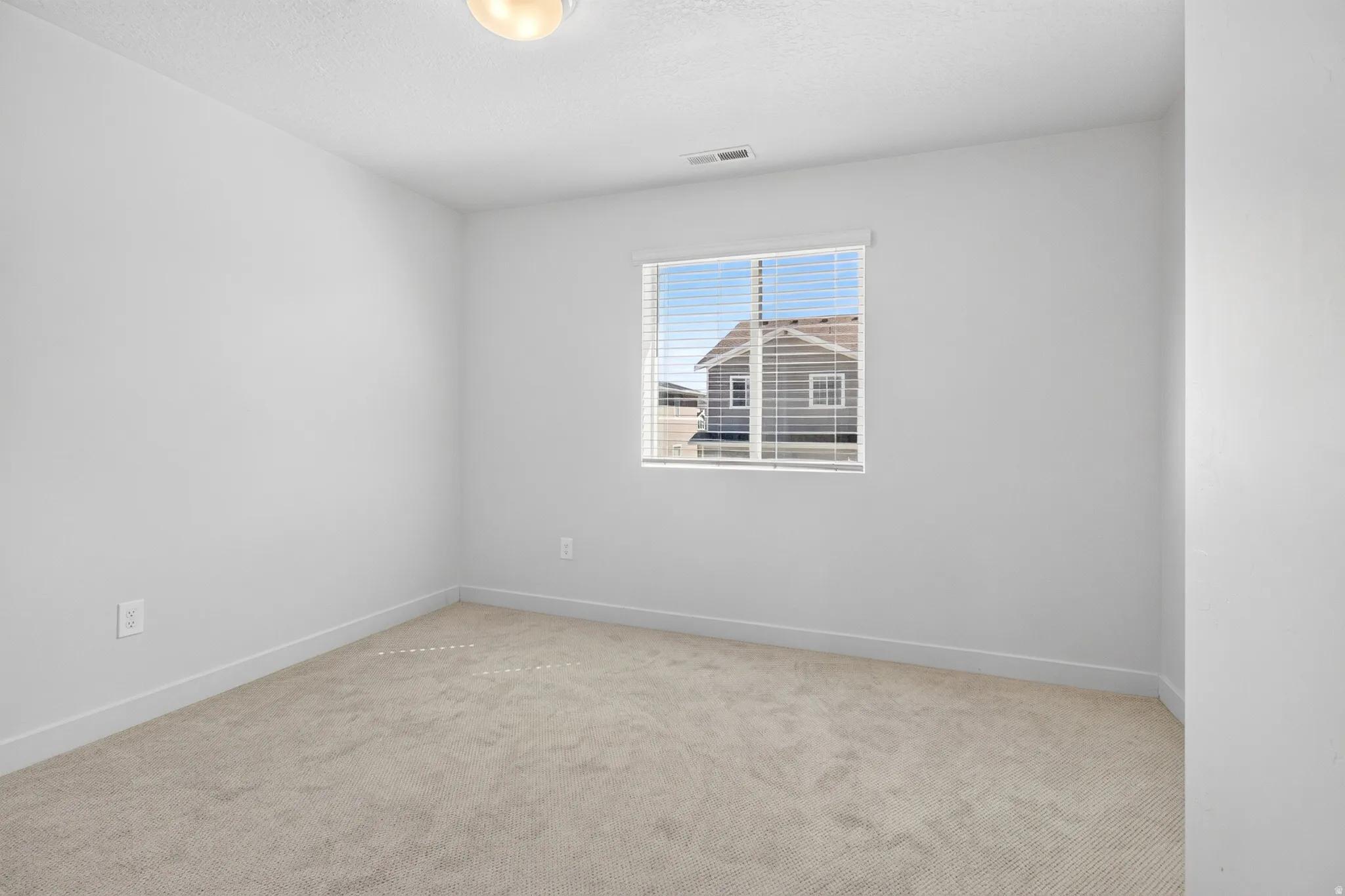 Light-filled room featuring neutral-toned carpeting, white walls, and a large window with blinds