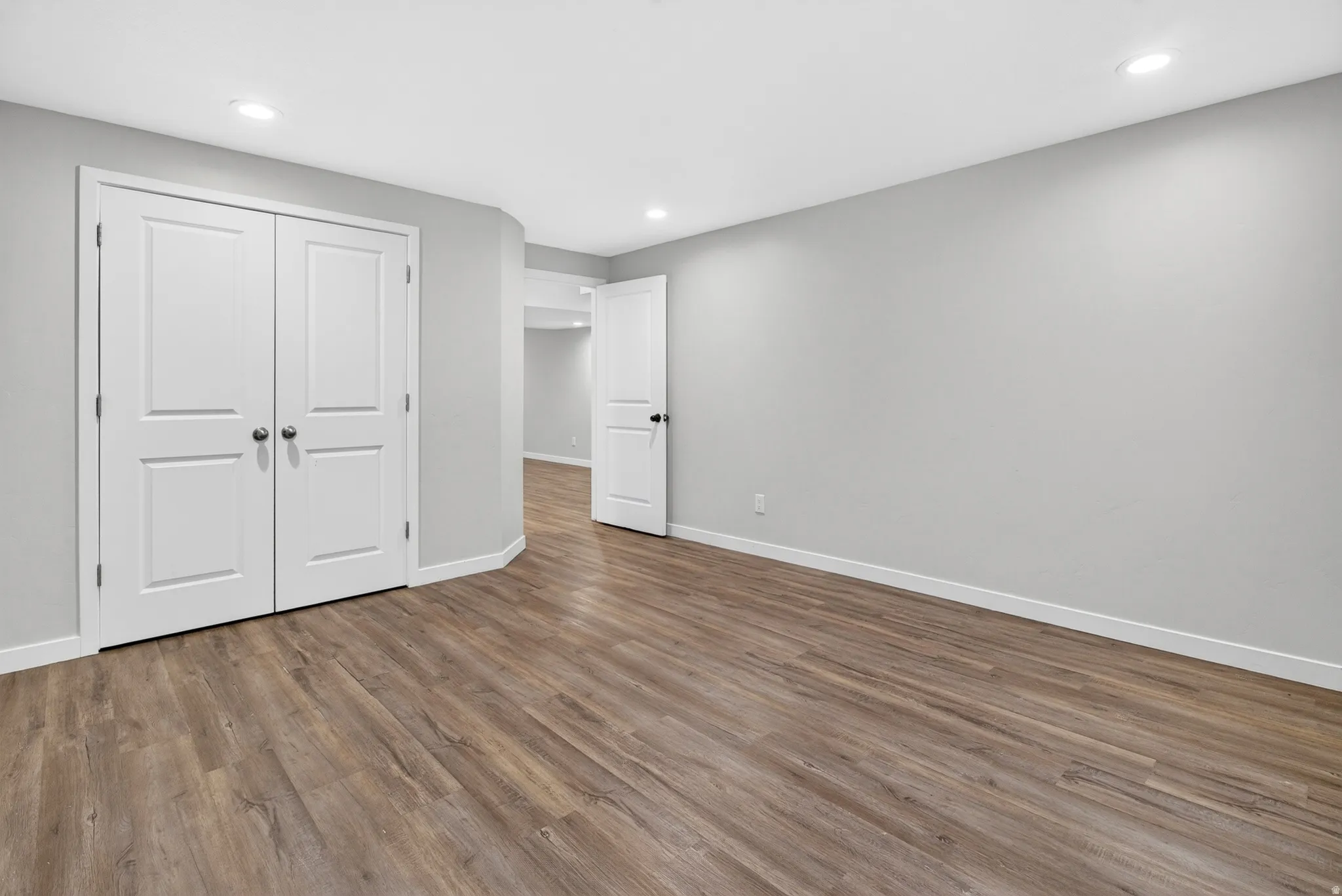 Spacious room with wood-finish flooring, light grey walls, and white baseboards