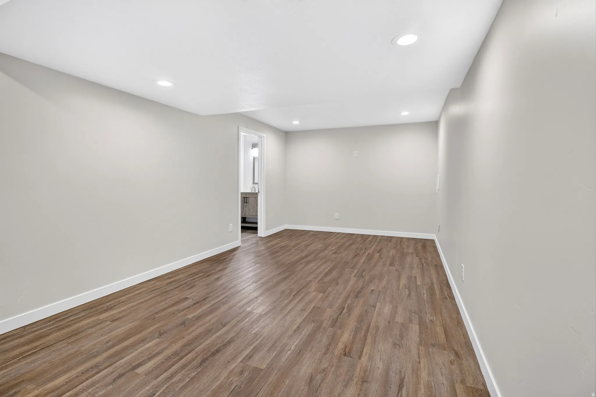 Spacious room featuring wood-finish flooring, light gray walls, white baseboards, and recessed ceiling lighting