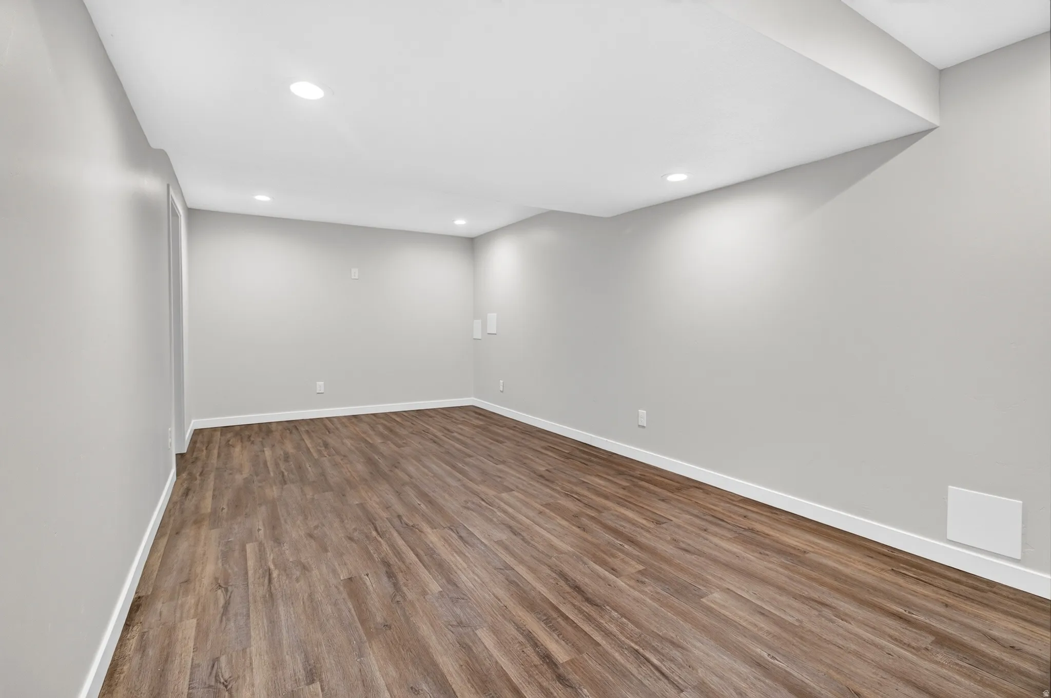 Spacious room featuring wood-finish flooring, recessed lighting, neutral gray walls, and white baseboards