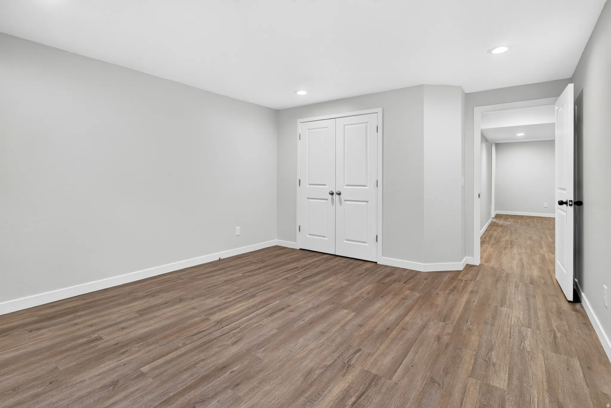 Spacious room featuring wood-finish flooring, light grey walls, white trim, and recessed lighting