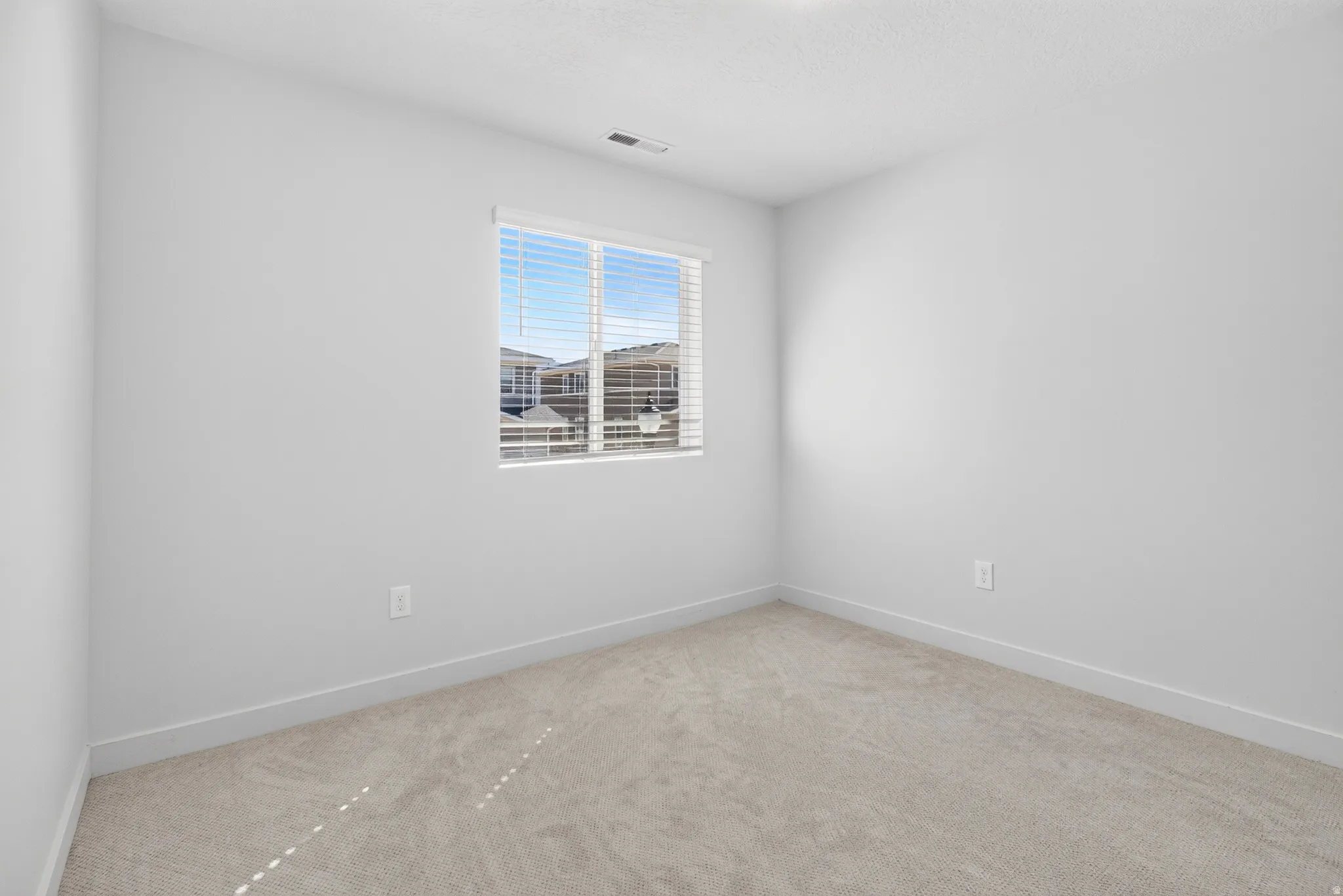 Light-filled room featuring neutral-toned carpeting, white walls, and a window with horizontal blinds