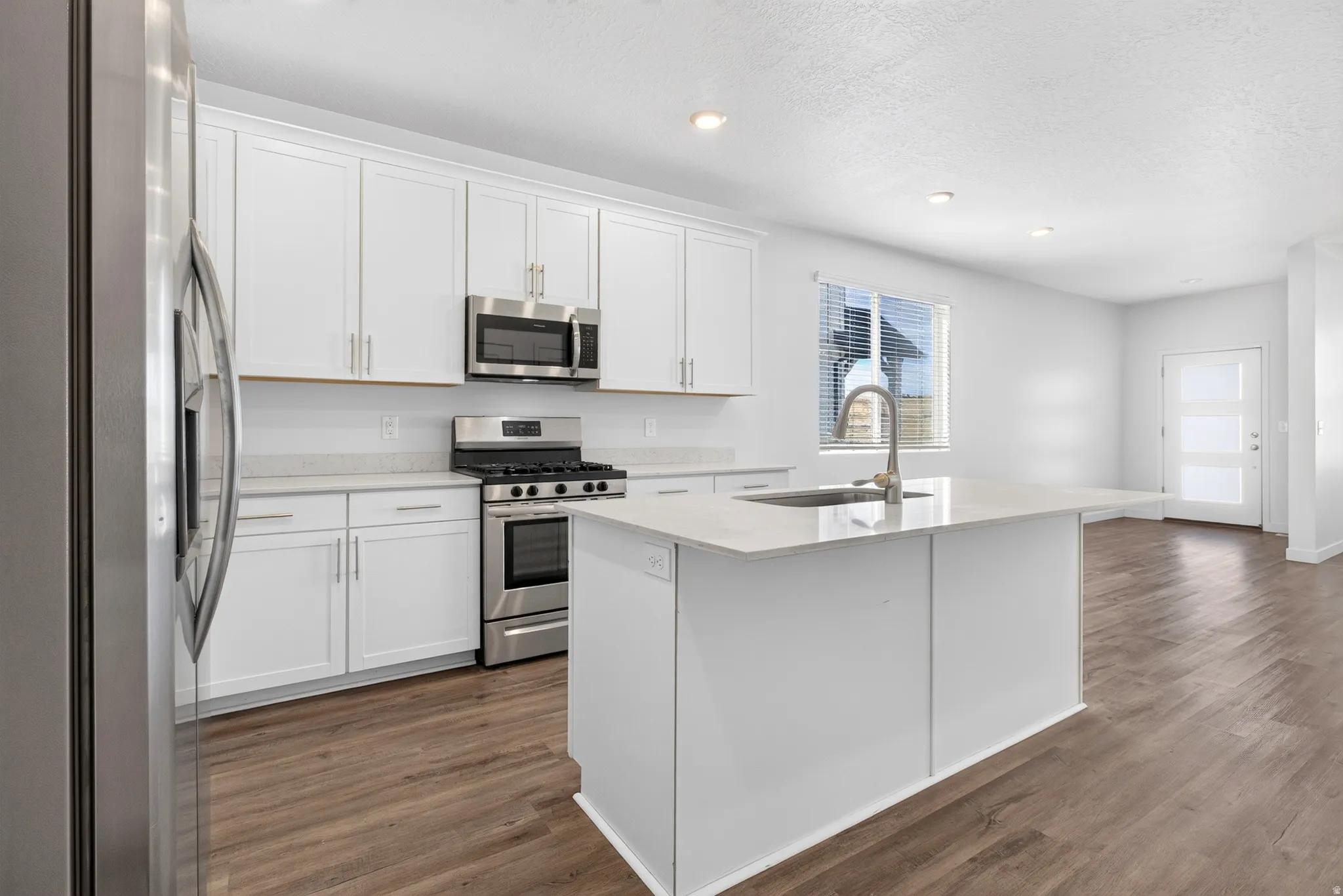 Modern kitchen featuring white cabinetry, stainless steel appliances, a white island with an integrated sink, and wood-finish flooring