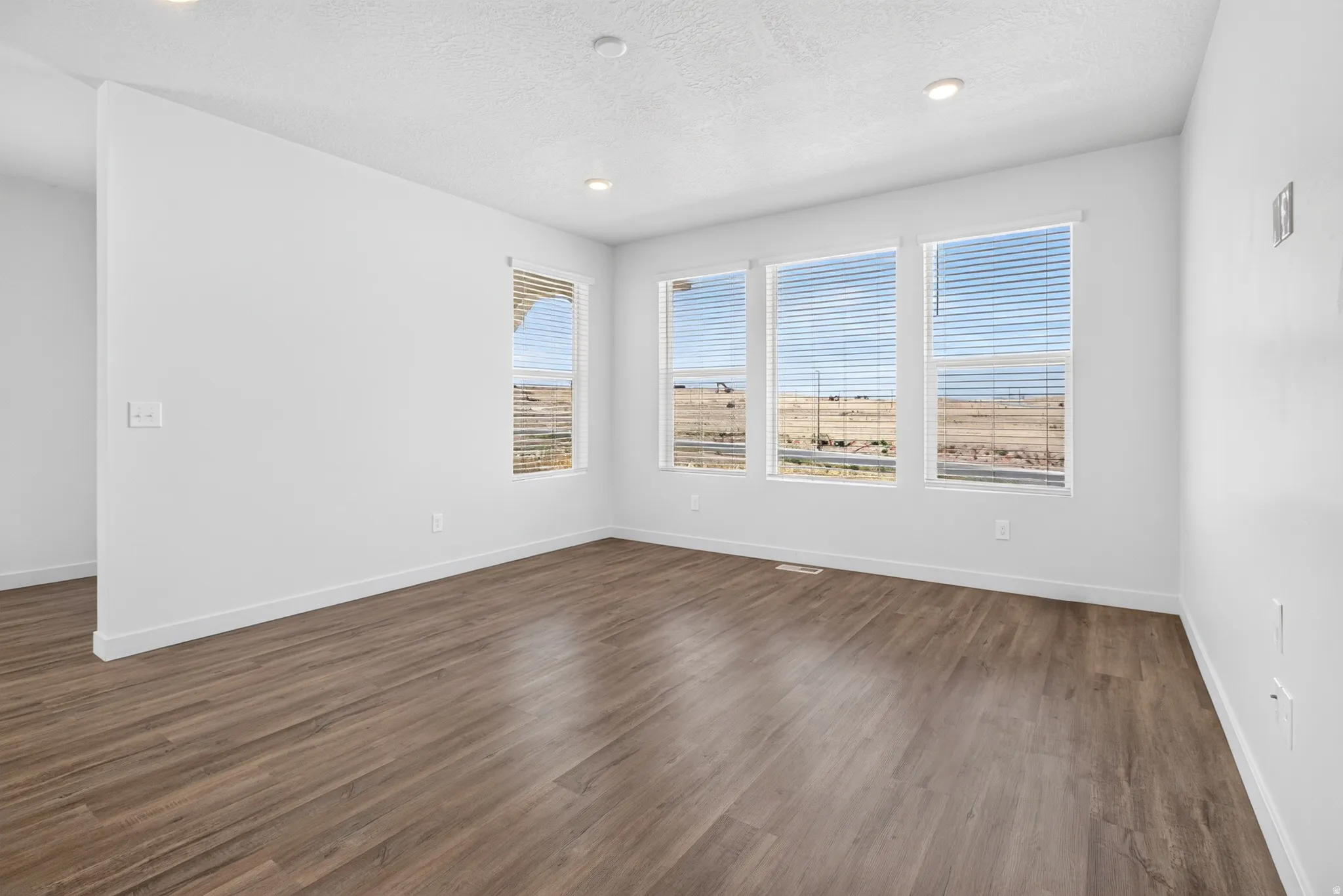 Spacious room featuring wood-finish flooring, white baseboards, and neutral wall paint