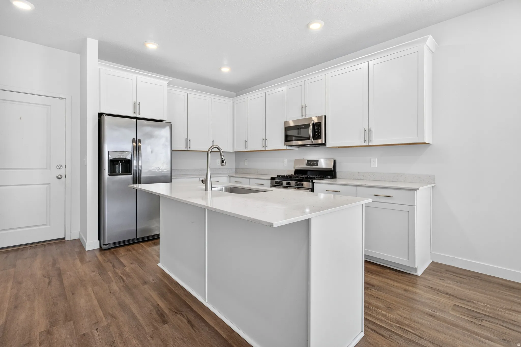 Modern kitchen featuring white cabinetry, a stainless steel appliance suite, a central island with a sink, quartz countertops, and wood-finish flooring