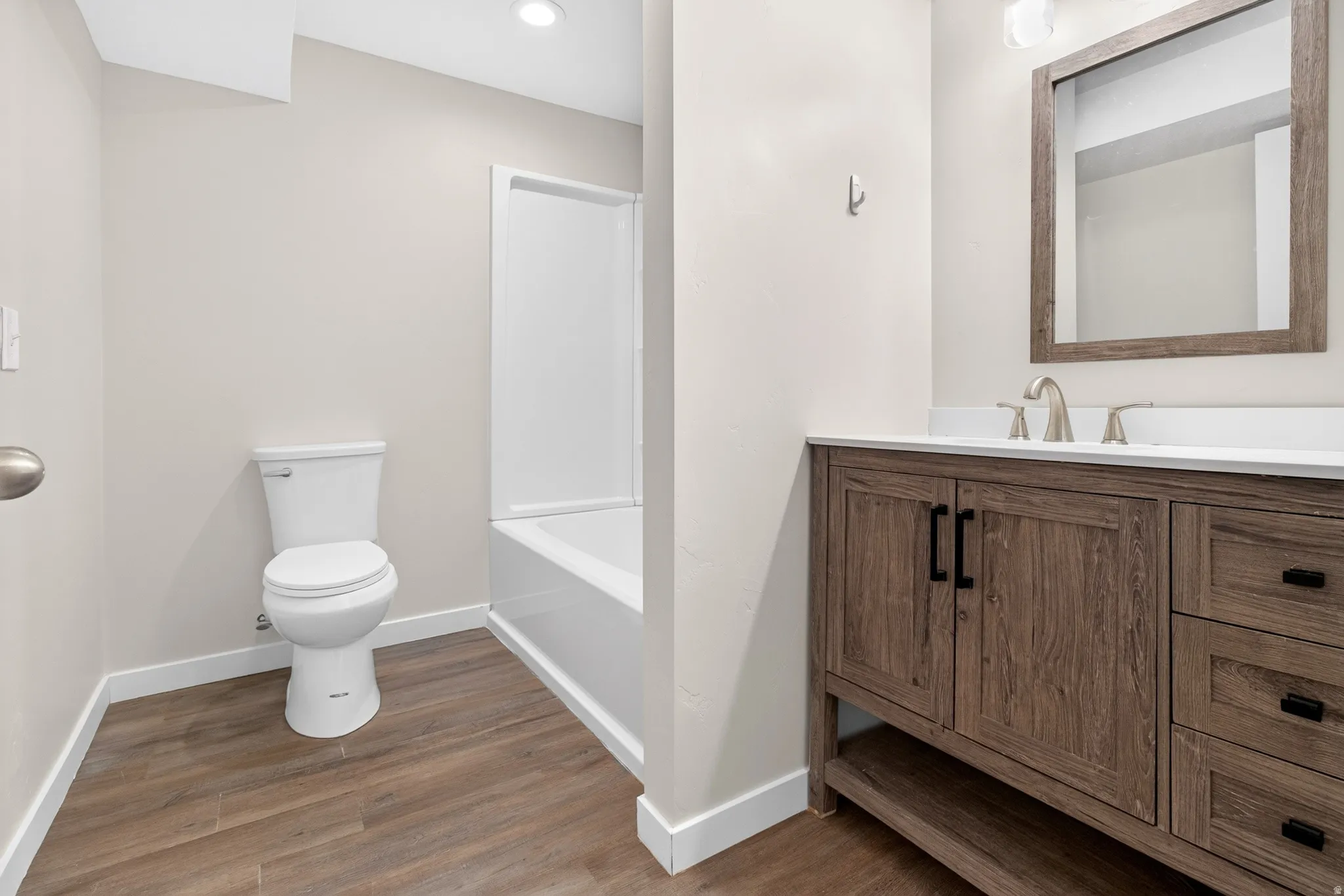 Bathroom featuring a wood-finish vanity with a white countertop, brushed nickel faucet, and framed mirror