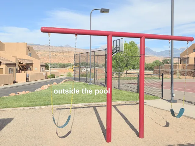 Community playground featuring a red swing set with two swings, a sandy ground cover, and a manicured grassy area