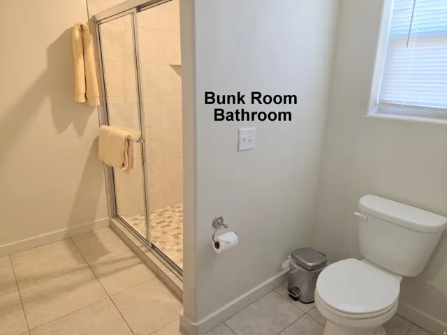 Tiled bunk bathroom featuring a glass-enclosed shower with pebble-finish flooring, a contemporary toilet, and a window with blinds