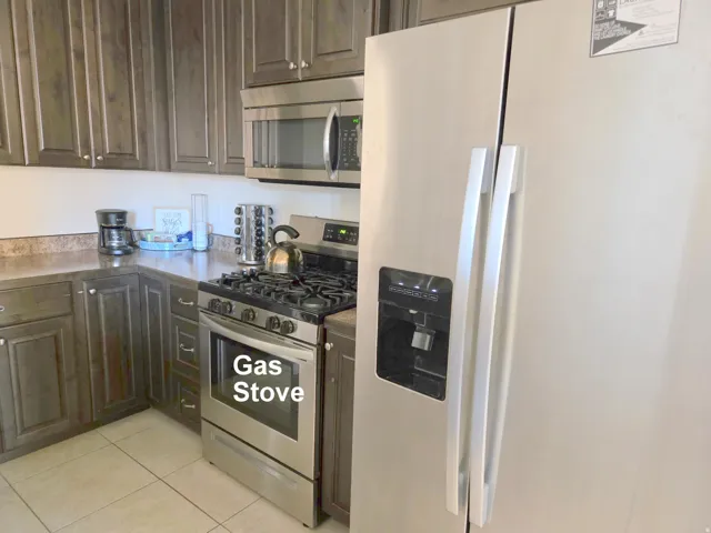 Kitchen showcasing extensive dark wood-finish cabinetry, stainless steel gas range, coordinating stainless steel microwave, and a side-by-side refrigerator with an external dispenser