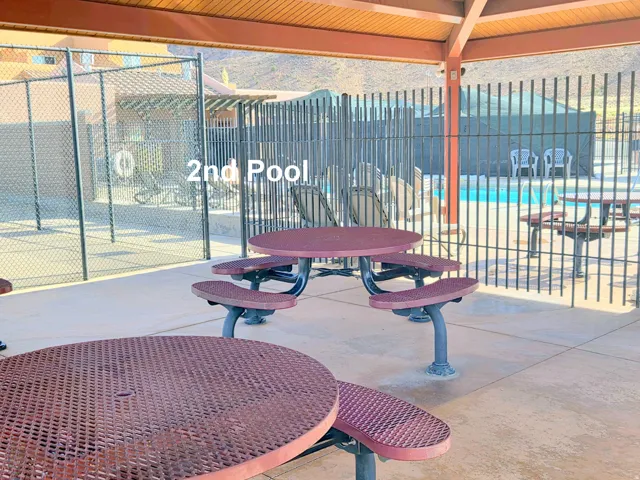 Covered patio area with concrete flooring, multiple picnic tables, a slatted wood ceiling, and a view of a fenced pool area
