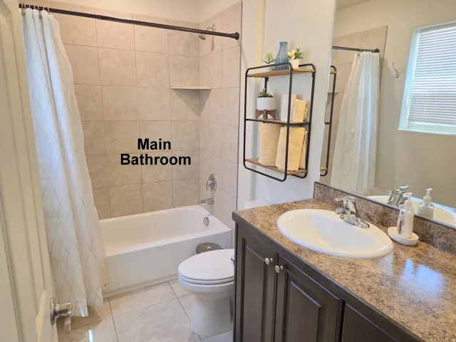 Bathroom featuring a shower-tub combination with tiled surround, a built-in shower niche, a vanity with an integrated sink, a large mirror, and a window with blinds