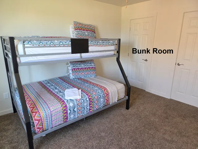 Carpeted room featuring a metal bunk bed frame with two sleeping levels, neutral-toned walls, and two white paneled doors