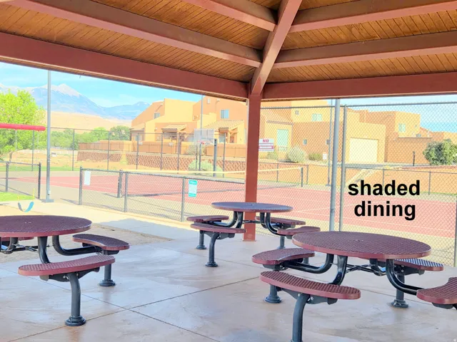 Covered outdoor dining area with multiple picnic tables, concrete flooring, and an exposed beam ceiling