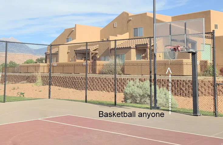 Fenced outdoor basketball court featuring a clear backboard and red court markings