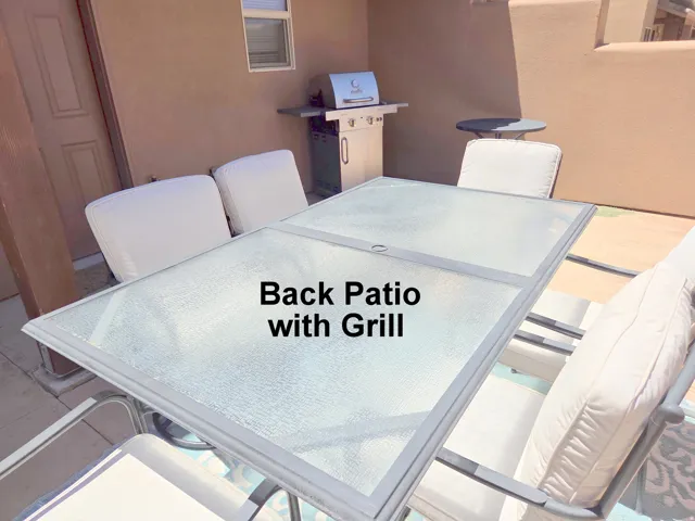 Spacious exterior patio featuring a glass-top table, integrated grill station, and stucco wall construction