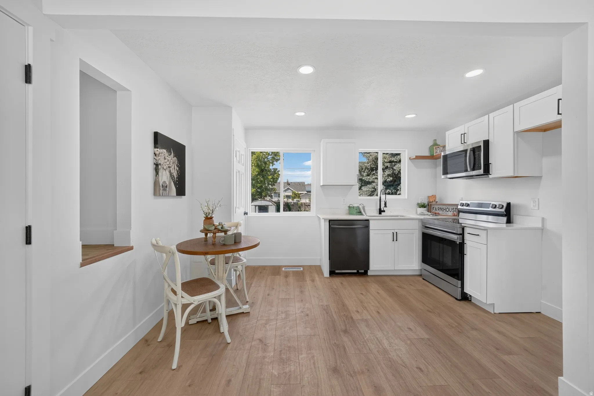 Modern kitchen featuring white cabinetry, stainless steel appliances, wood-finish flooring, recessed lighting, and a window over the sink