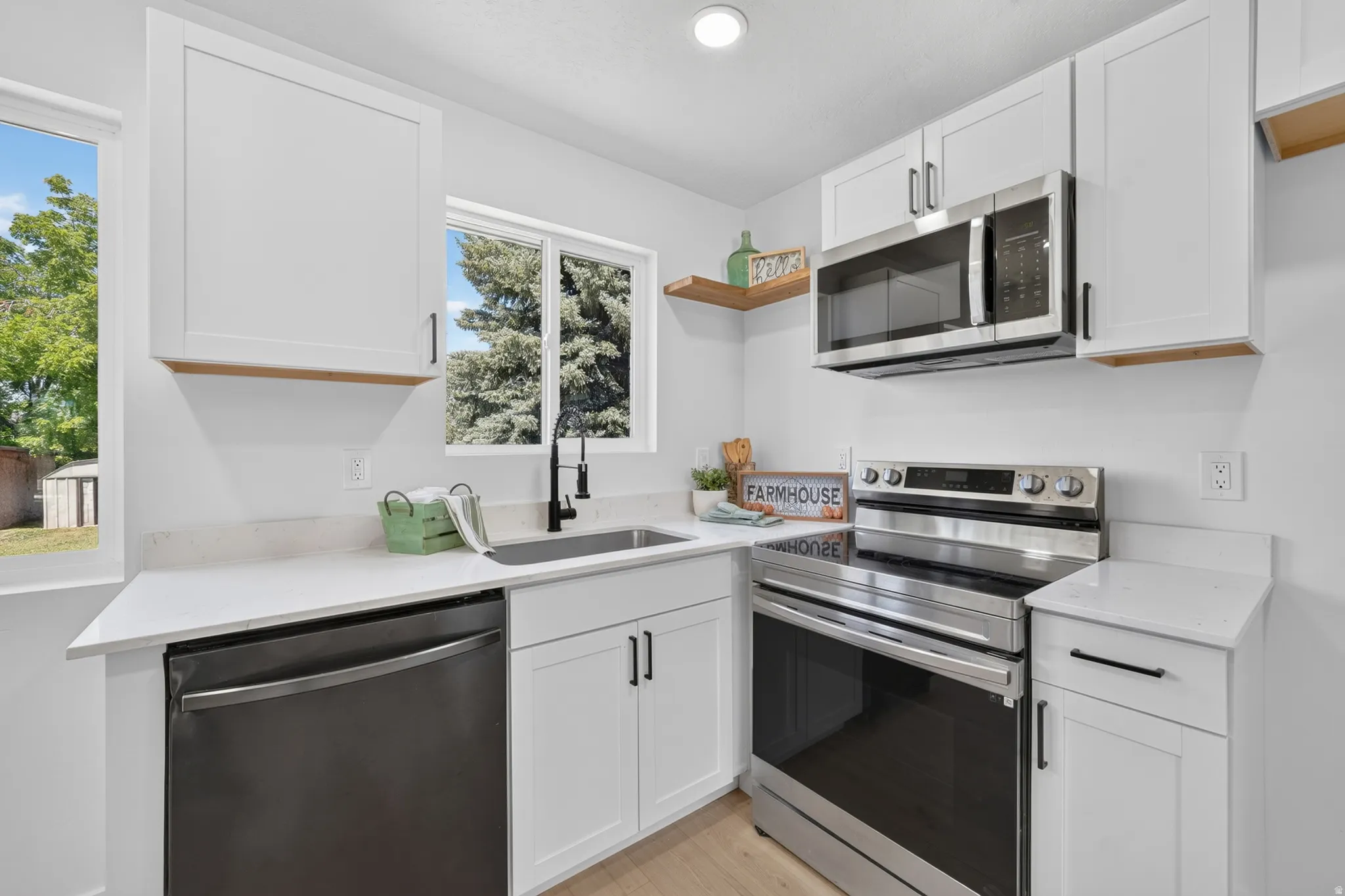 Bright kitchen featuring white shaker cabinetry, stainless steel appliances, quartz countertops, and a black gooseneck faucet