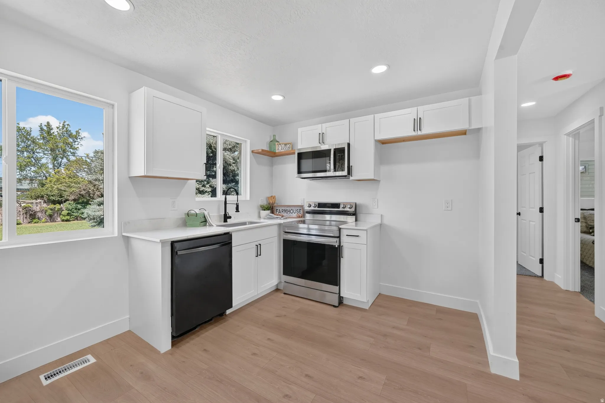 Modern kitchen featuring wood-finish flooring, white cabinetry, stainless steel appliances, and quartz countertops