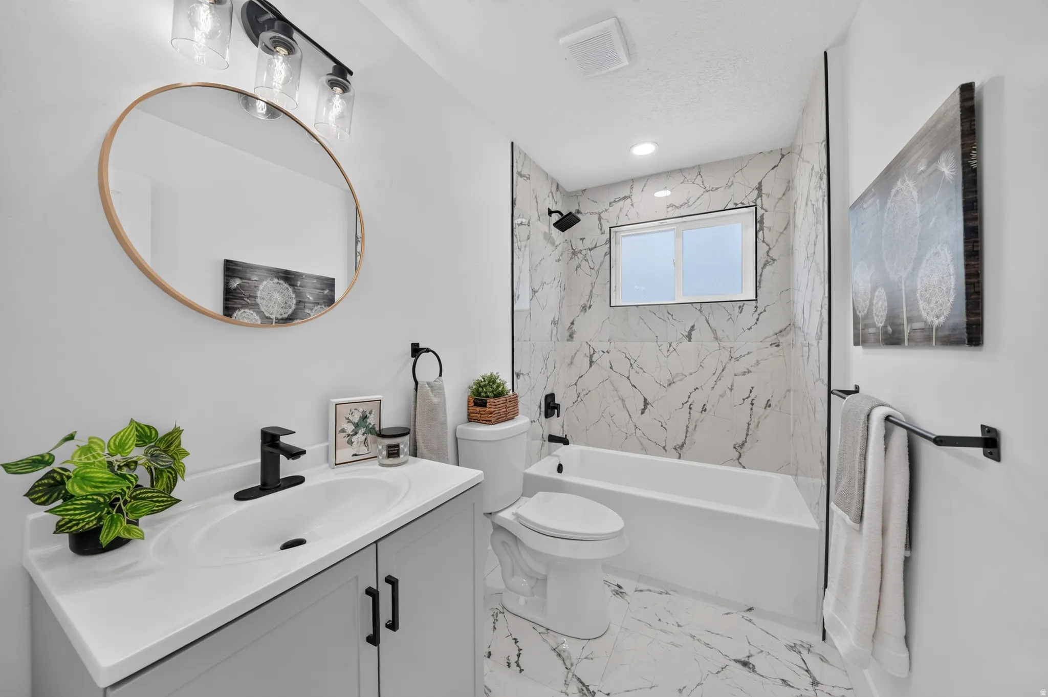 Bathroom featuring a white vanity with integrated sink, black fixtures, round framed mirror, and a black-framed light fixture