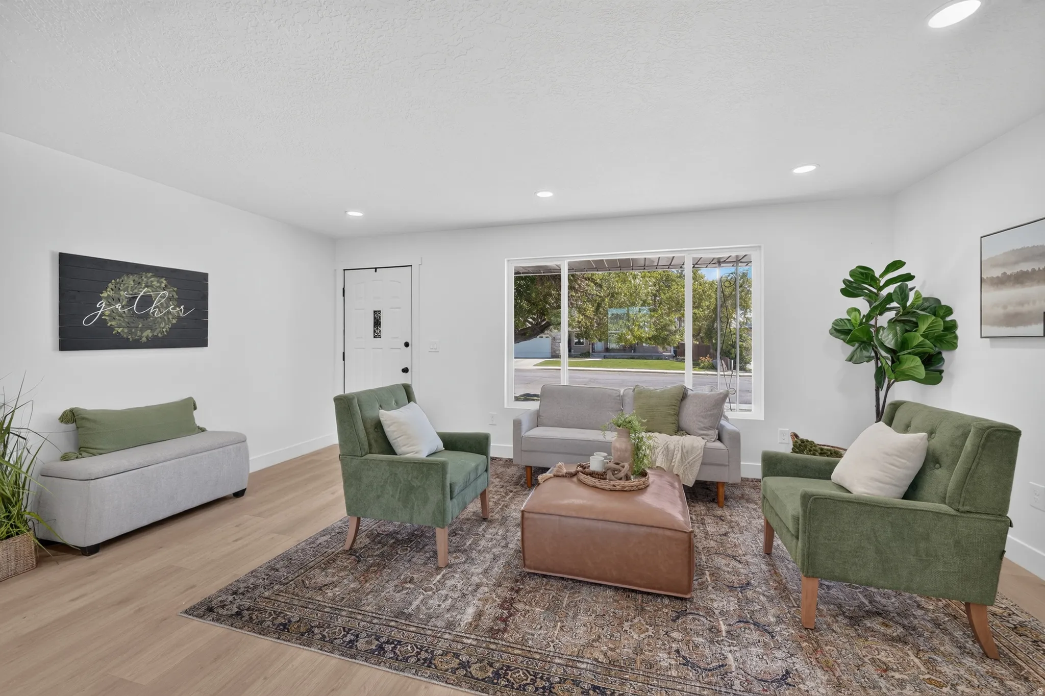 Spacious living area featuring light wood-finish flooring, a contemporary white entry door with a frosted glass insert, and recessed ceiling lighting